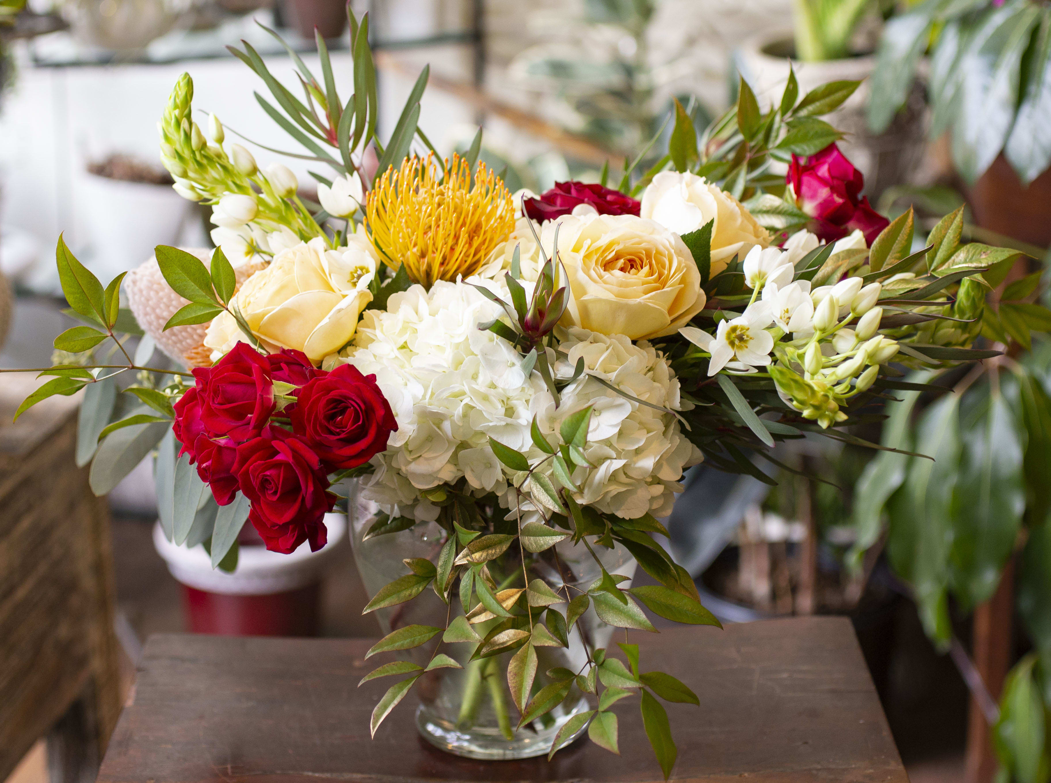 Aurelia - Romantic, warm flowers in reds, creams and whites, arranged in a clear glass vase.
