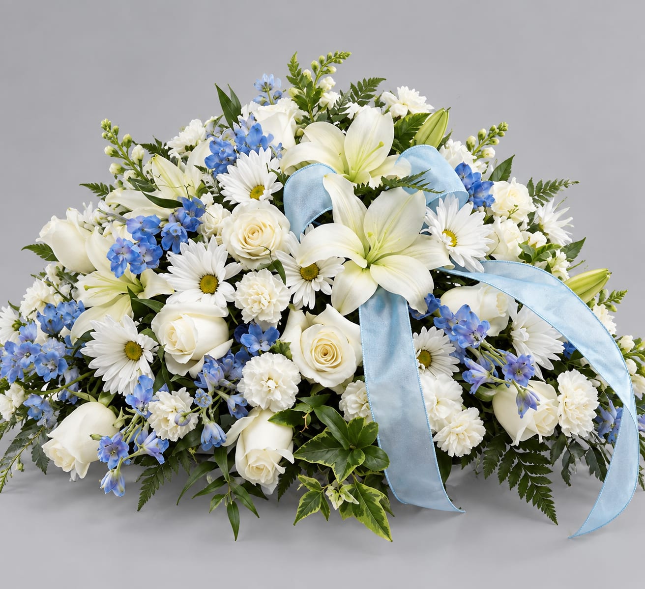 White lilies, roses, and blue flowers arranged with a light blue ribbon