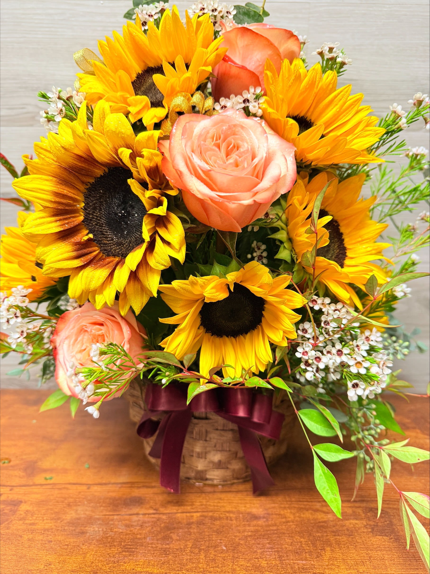 Basket arrangement of sunflowers and peach roses with small white filler flowers