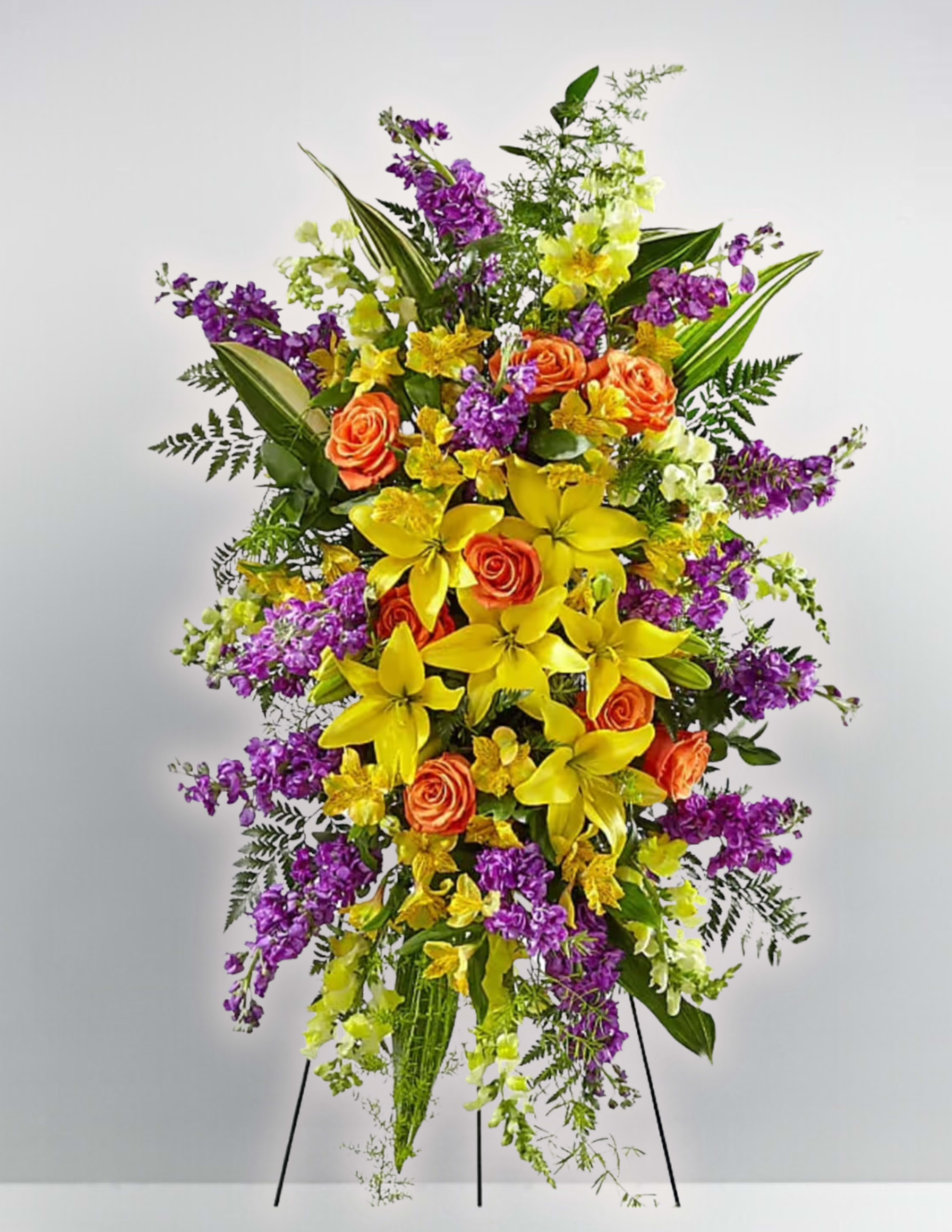 Tall floral standing spray with yellow lilies, orange roses, and purple blooms