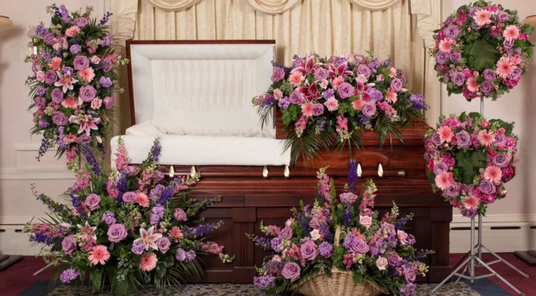 Funeral casket surrounded by purple and pink floral sprays and wreaths