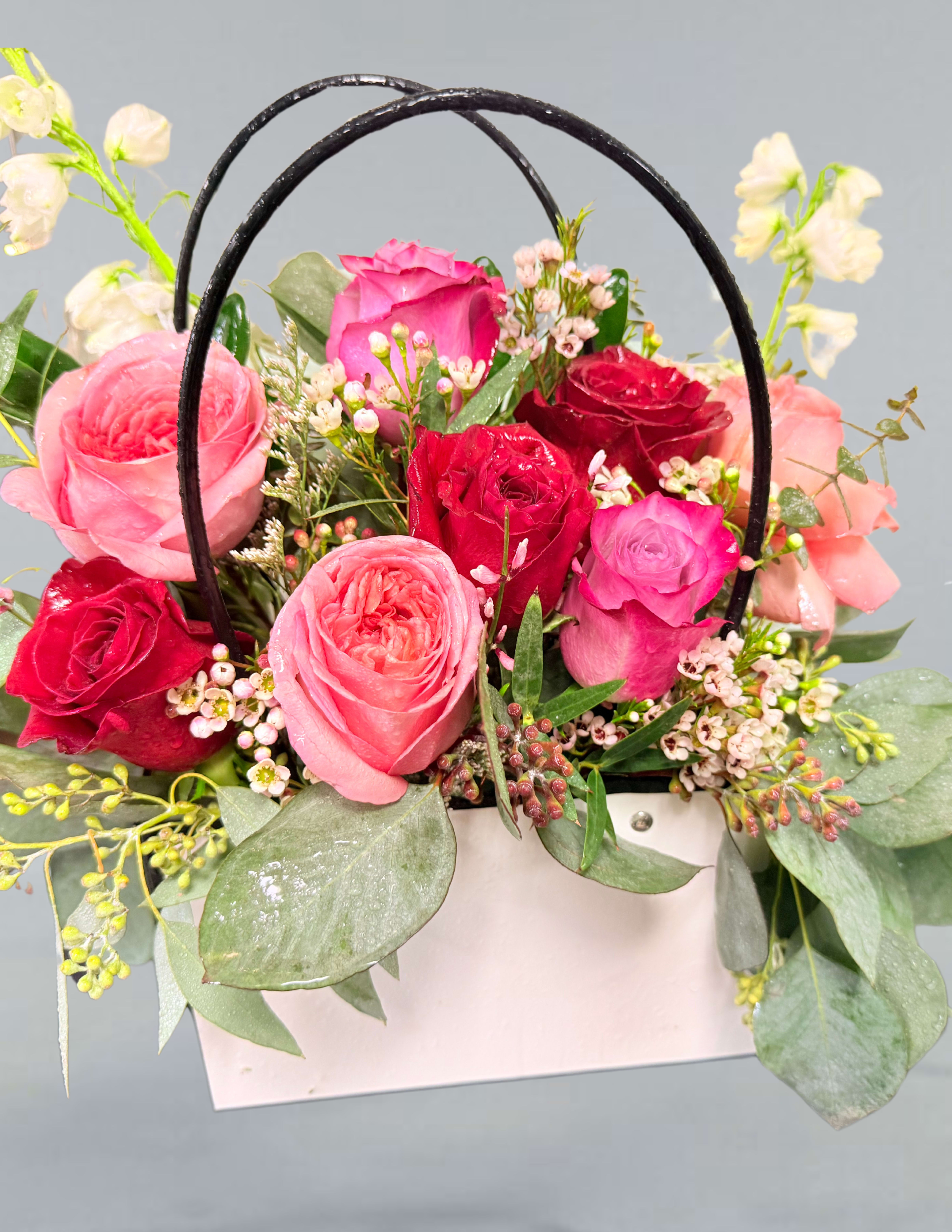 Pink and red roses arranged in a white basket with black handles