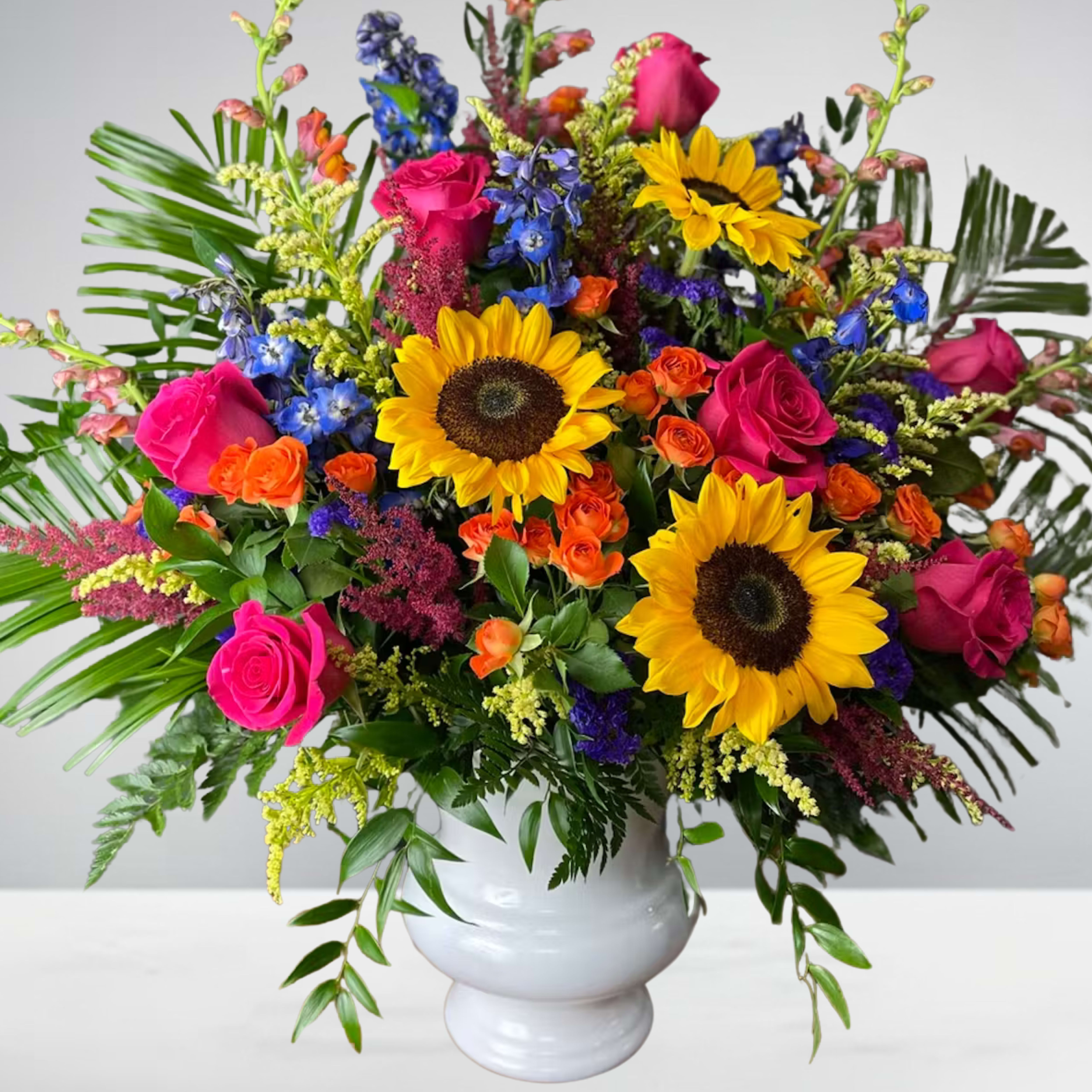 Colorful bouquet with sunflowers, pink roses, and blue flowers in a white vase