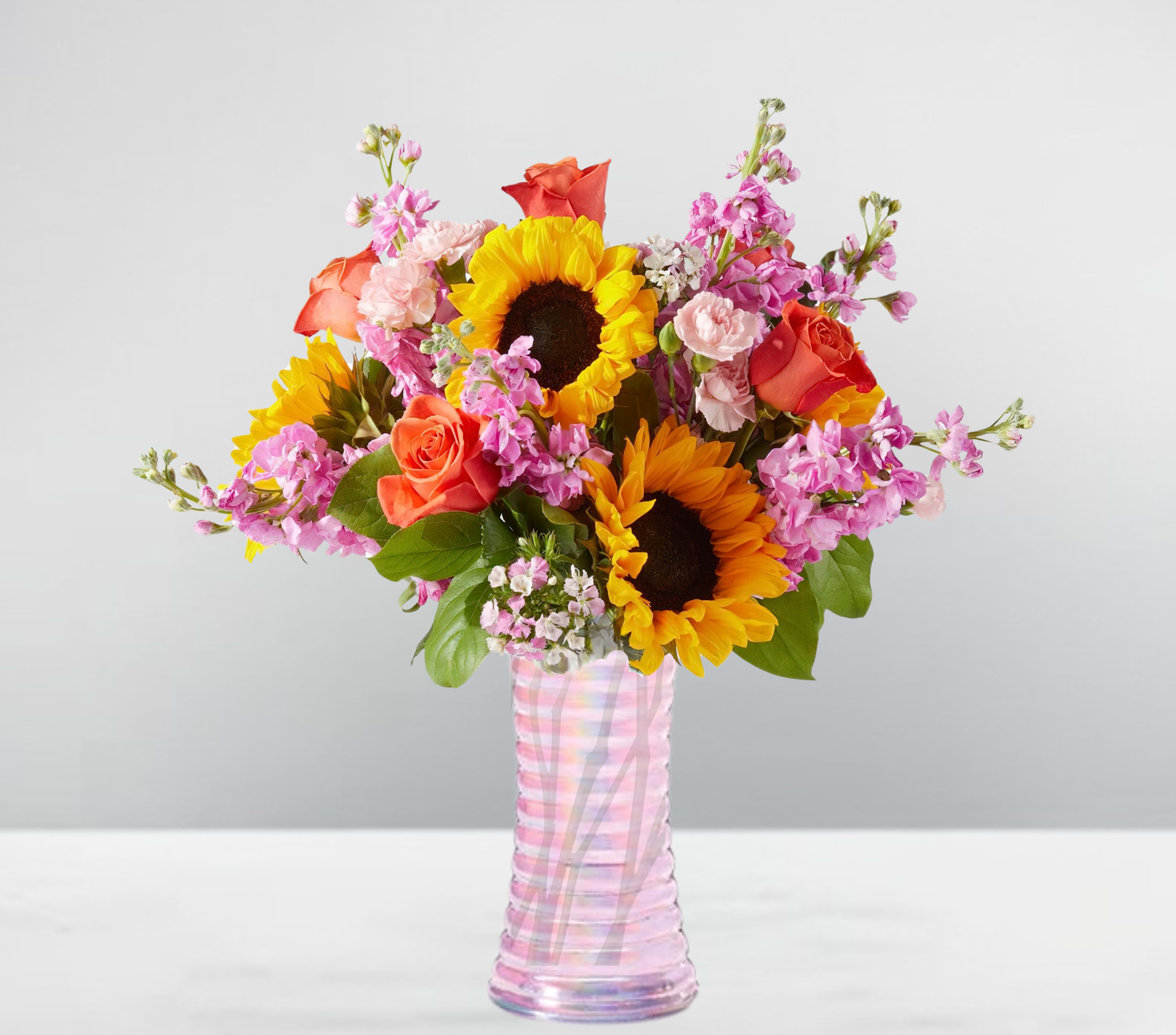 Bouquet of sunflowers, roses, and pink flowers in a striped glass vase