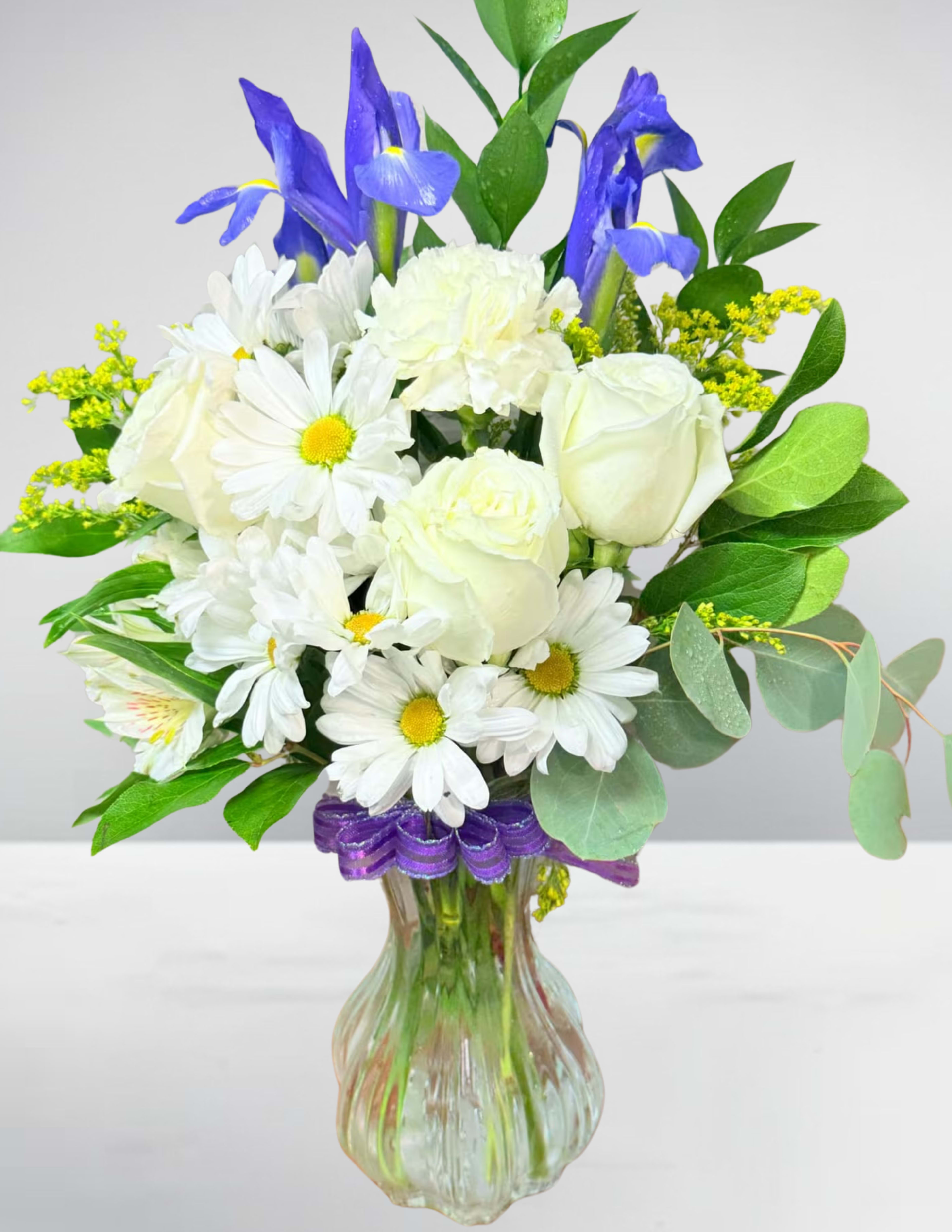 White roses and daisies with blue irises in a glass vase
