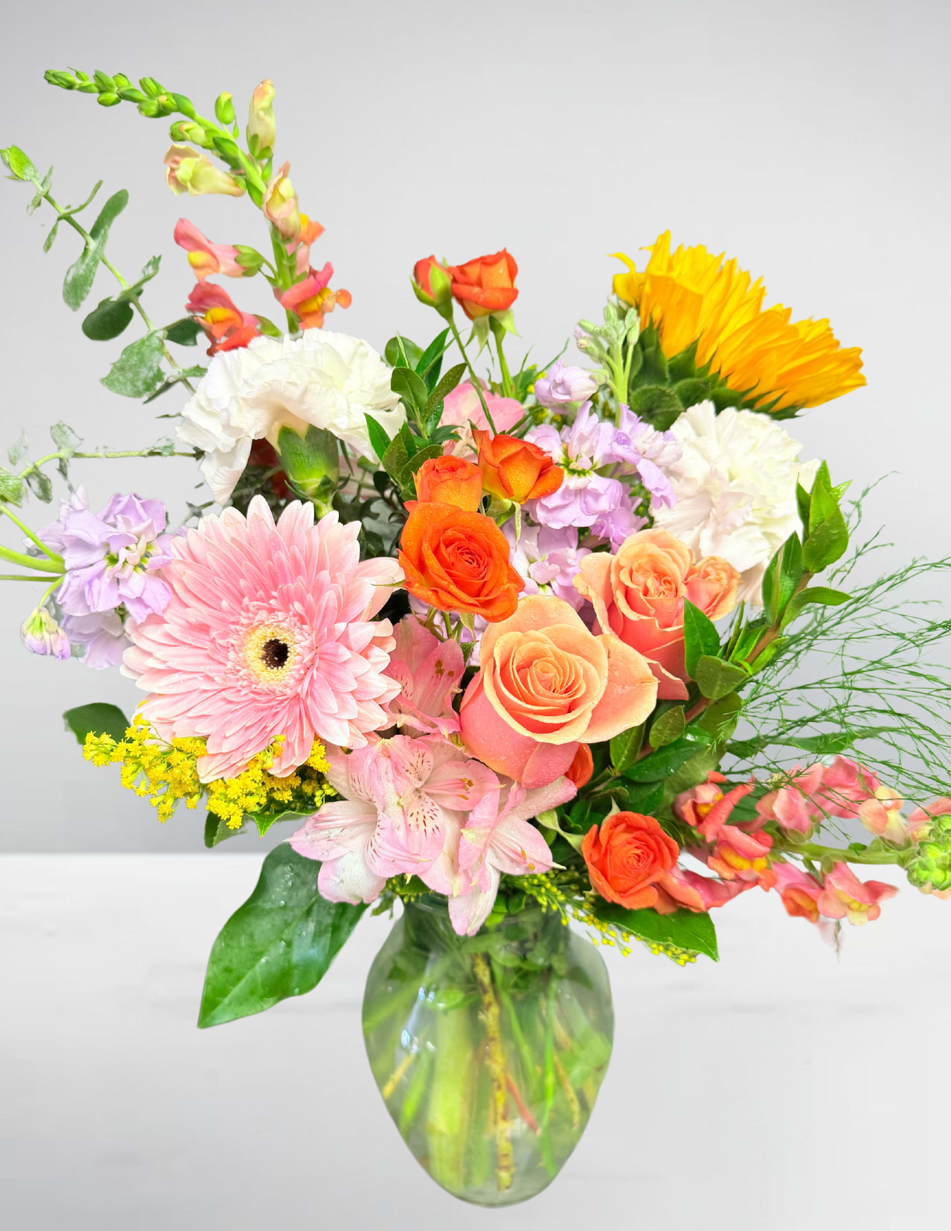 Mixed bouquet of pink, orange, yellow, and white flowers in a glass vase