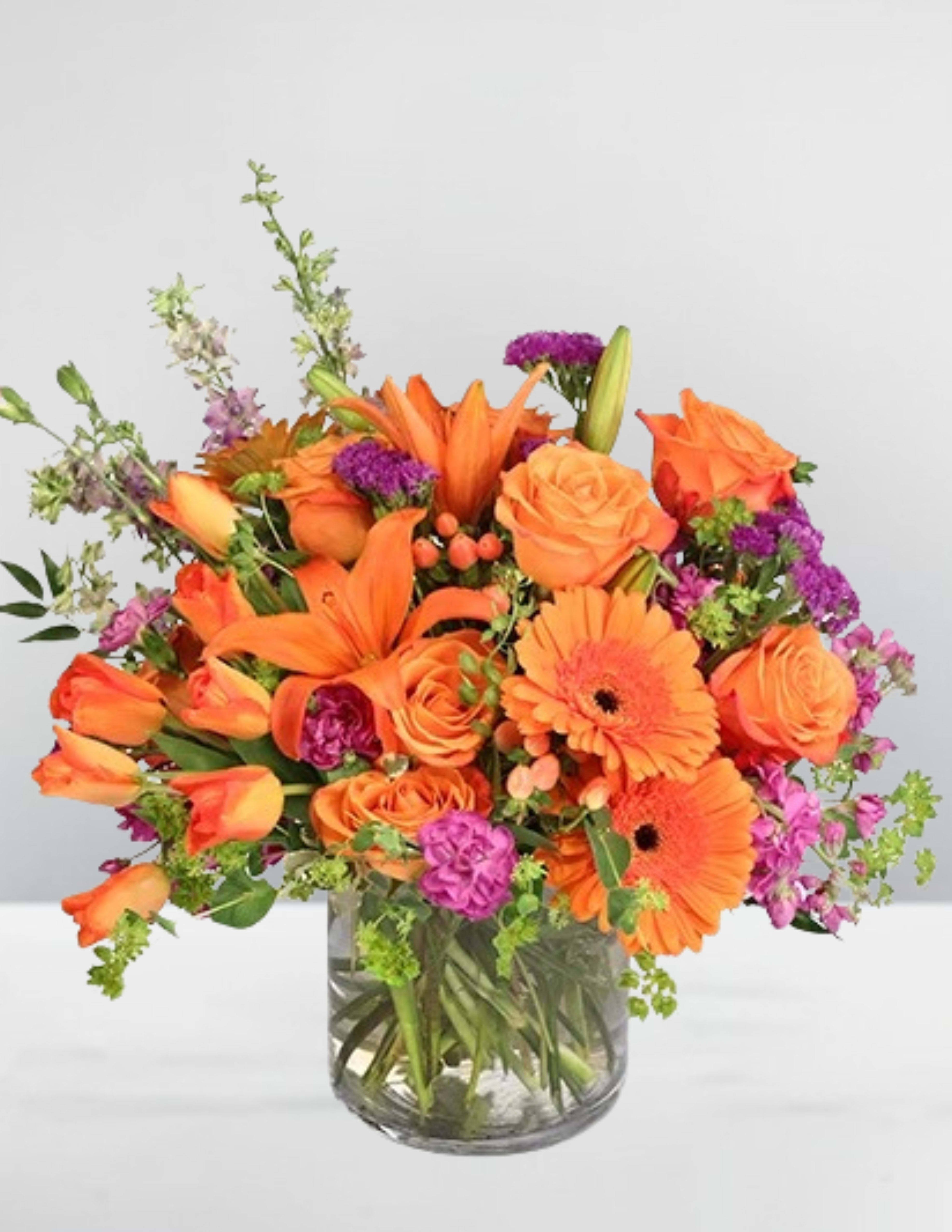 Orange flowers in a clear glass vase with purple accents