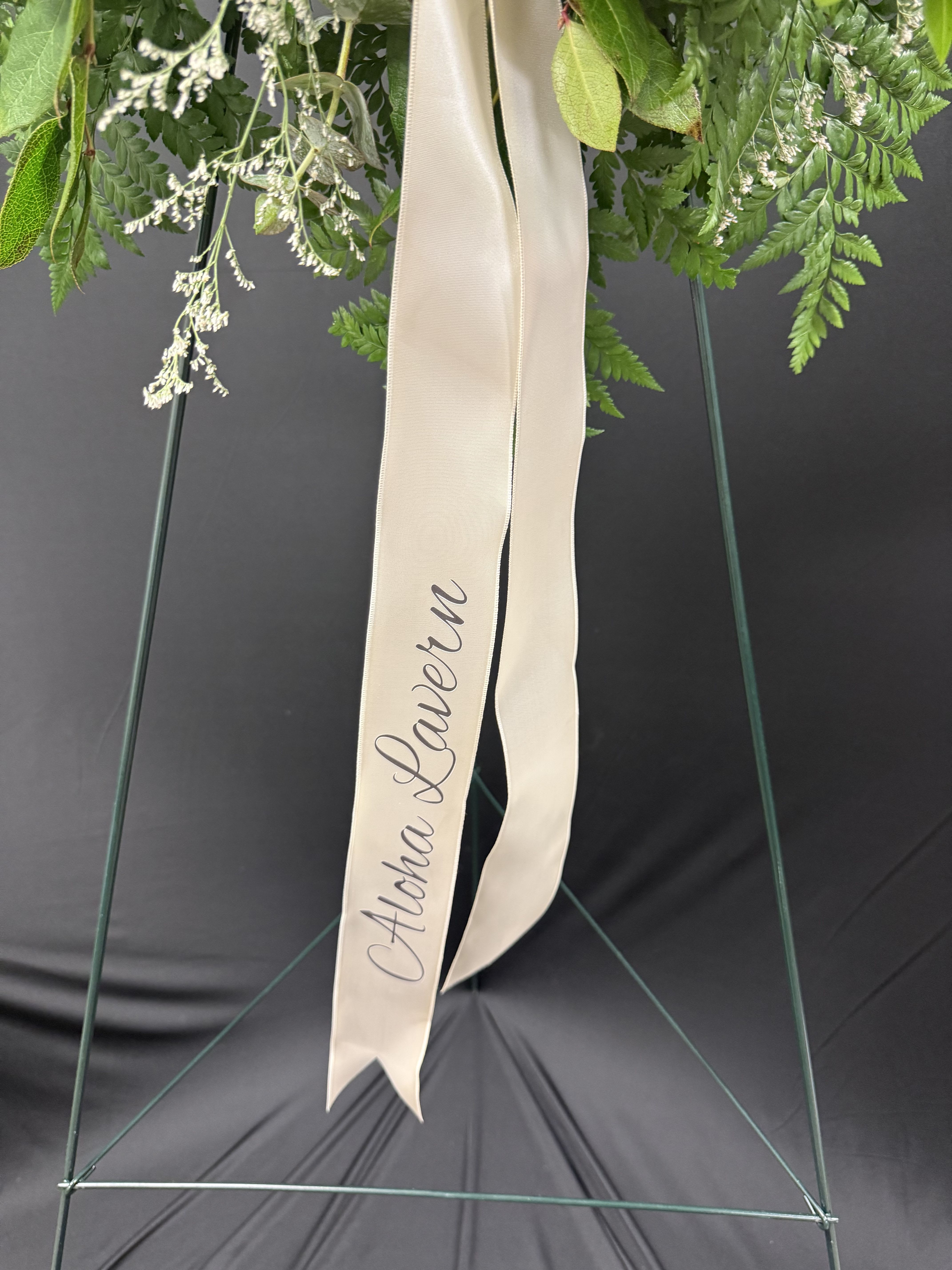 Green floral wreath with a cream ribbon reading "Aloha Lauren"