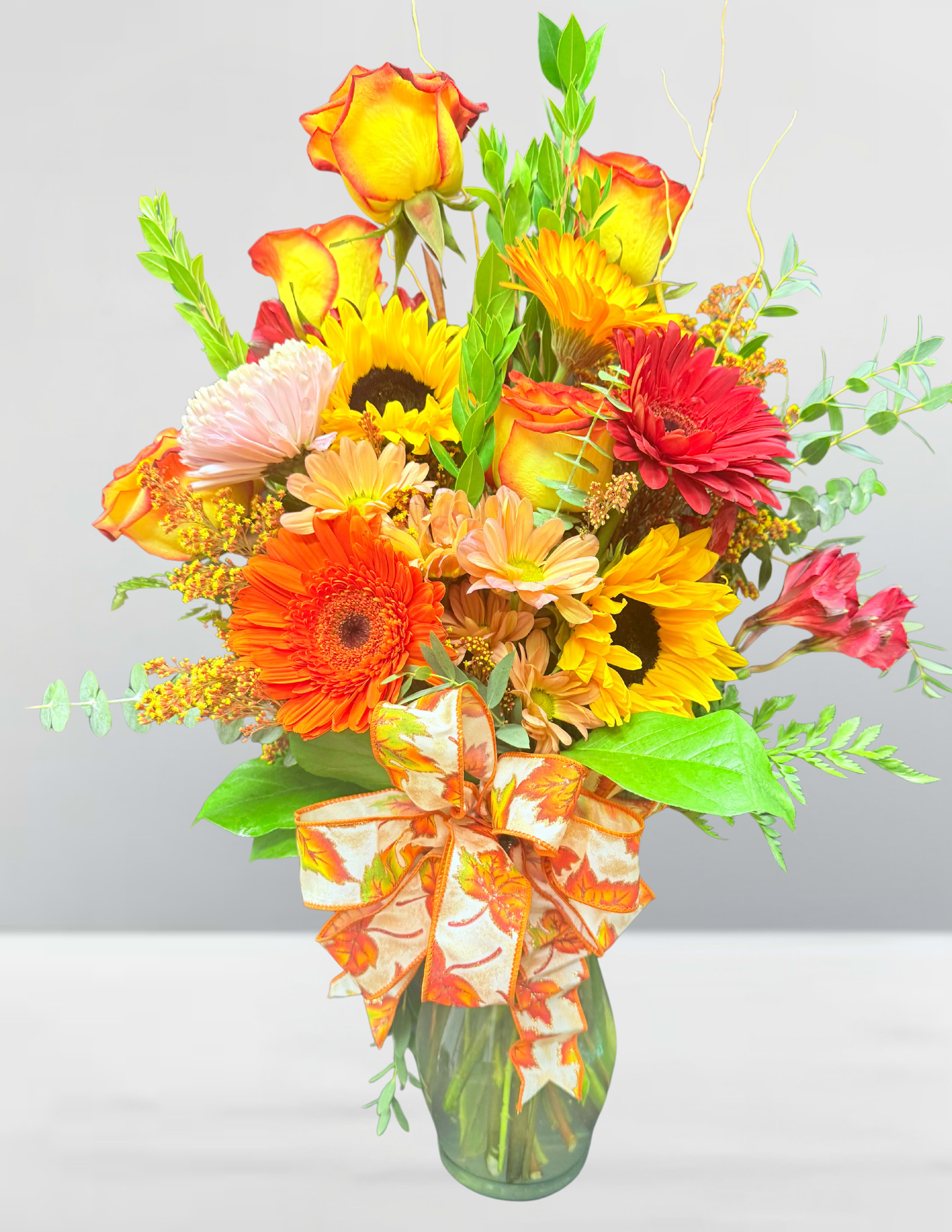 Bouquet of mixed autumn flowers in a glass vase with a patterned ribbon
