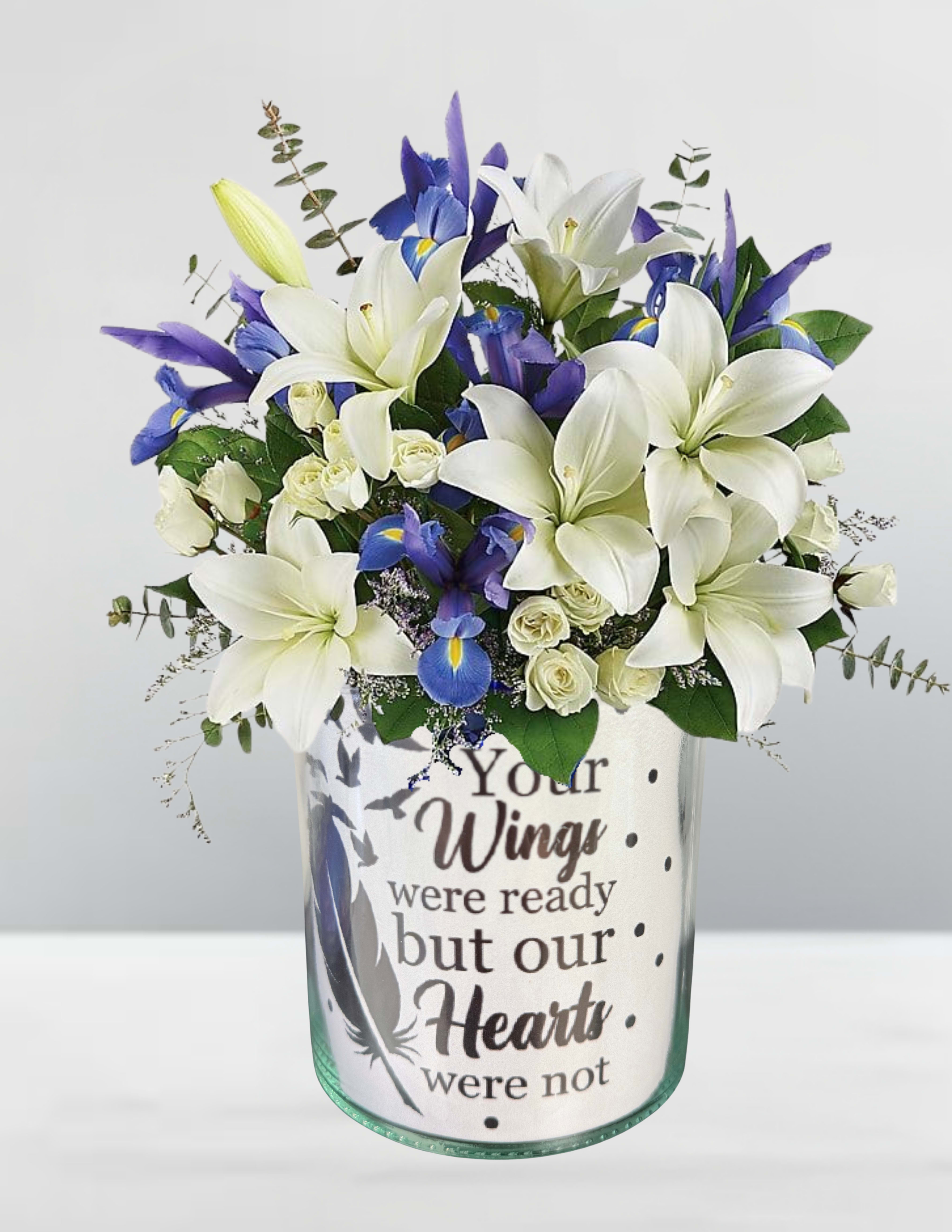 White lilies and blue irises in a glass vase with a memorial message
