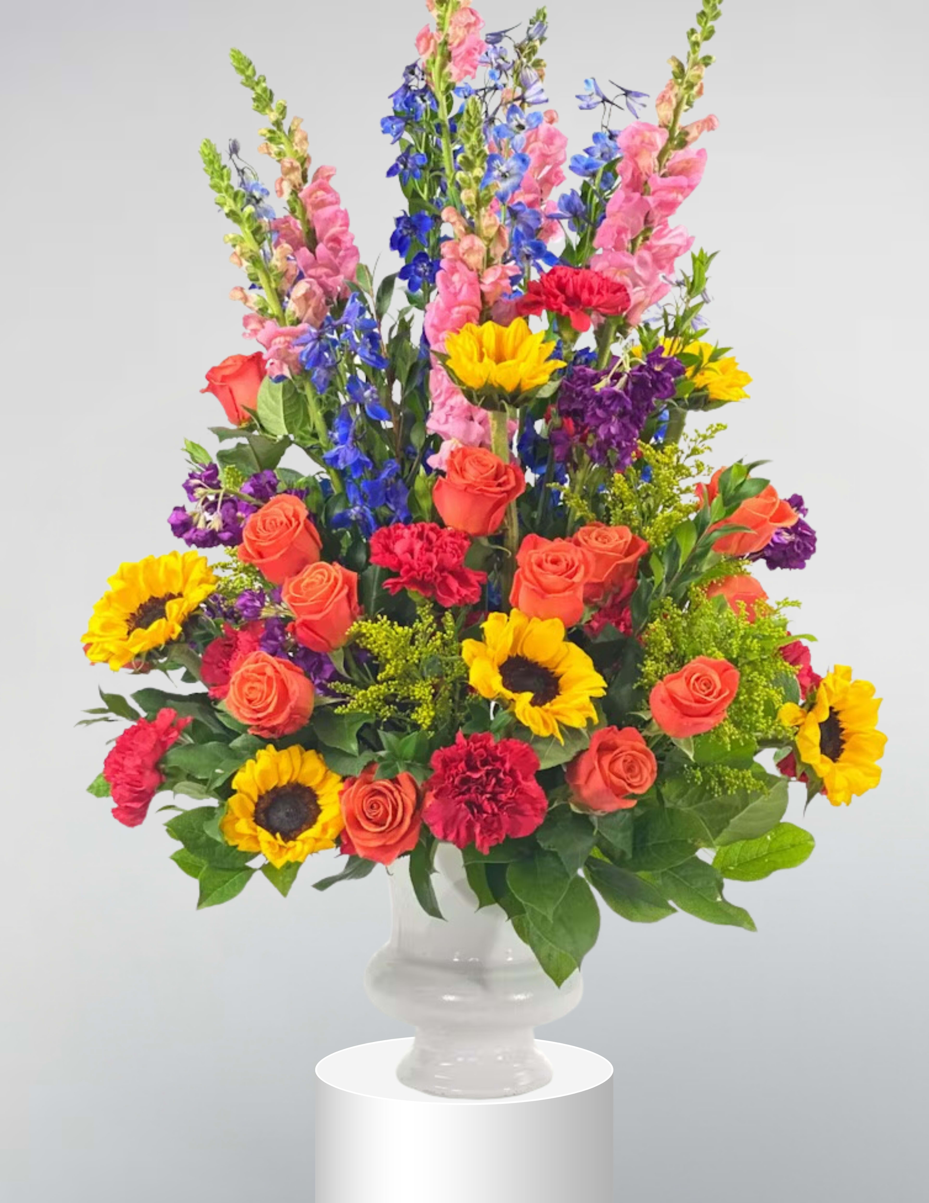 Colorful mixed bouquet in a clear glass vase with roses, sunflowers, and tall blue blooms