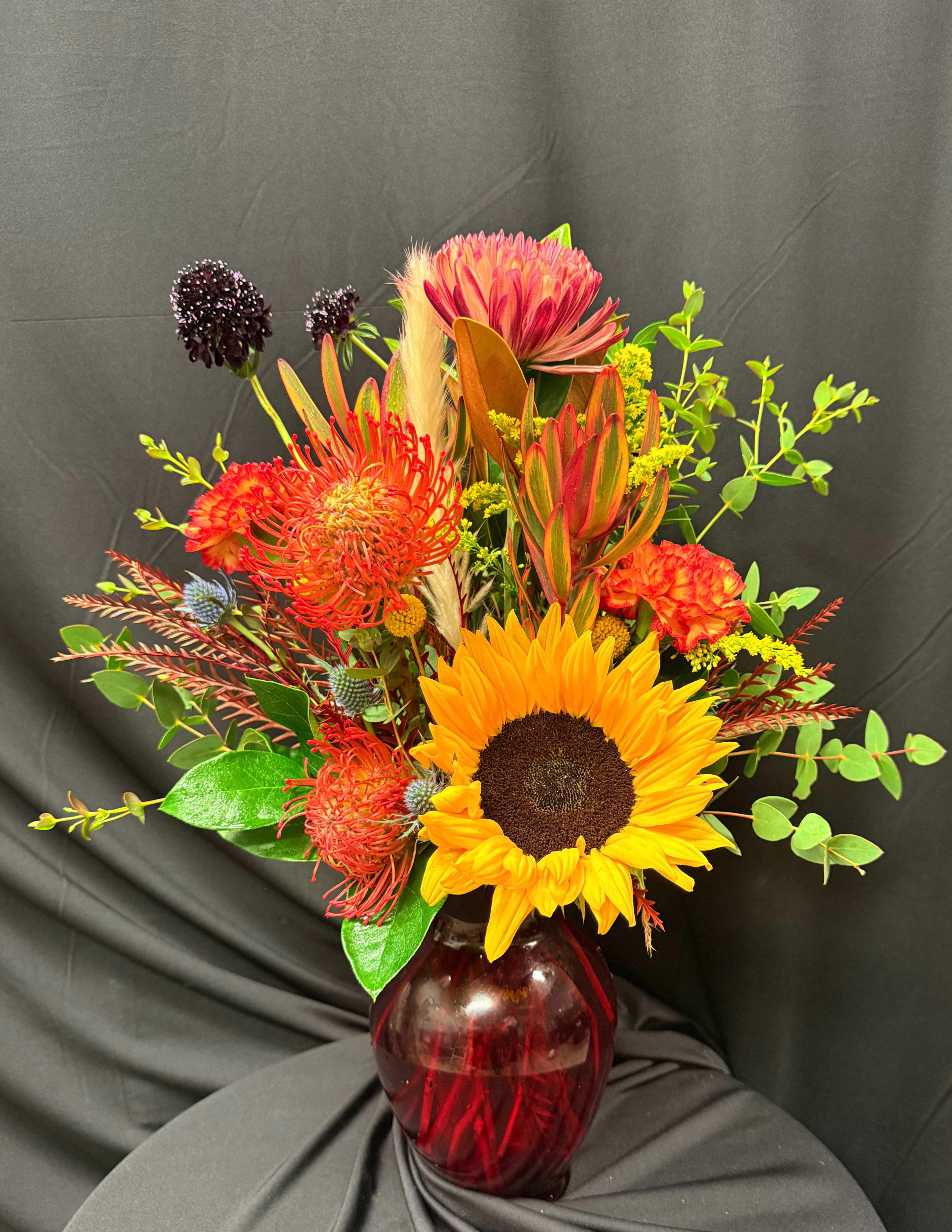 Bright mixed bouquet with a sunflower in a red glass vase