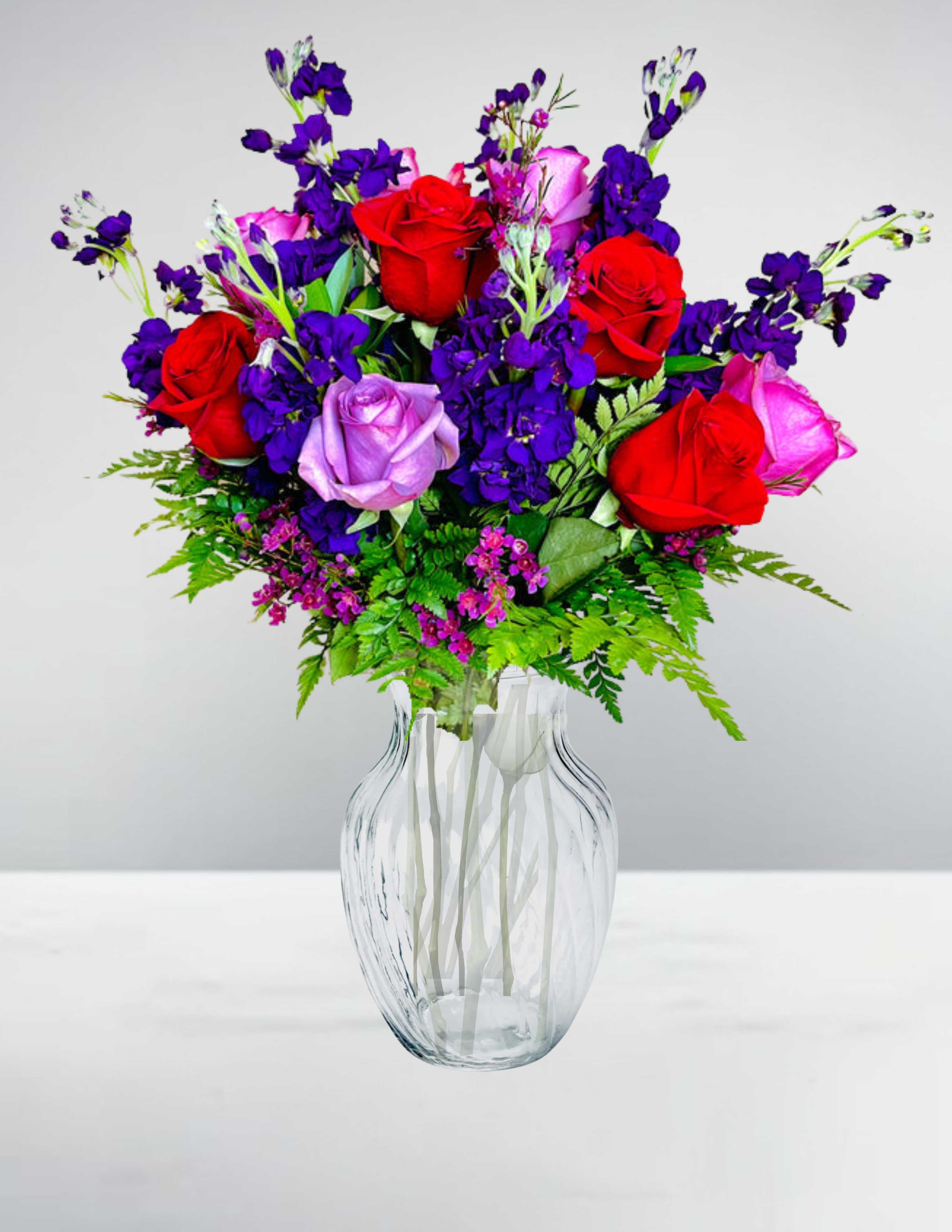 Bouquet of red, pink, and lavender roses in a clear glass vase