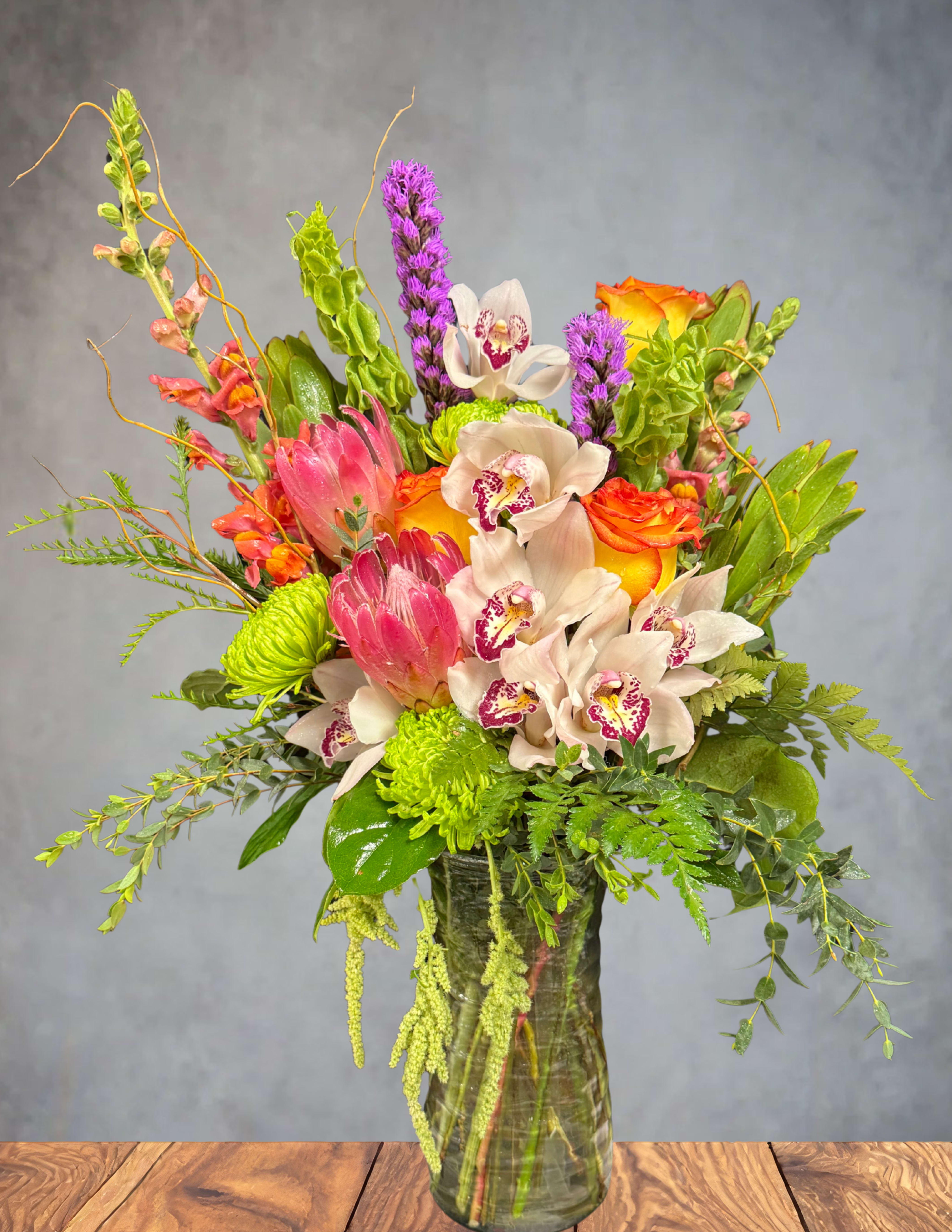 Mixed bouquet with orchids, roses, and green blooms in a glass vase