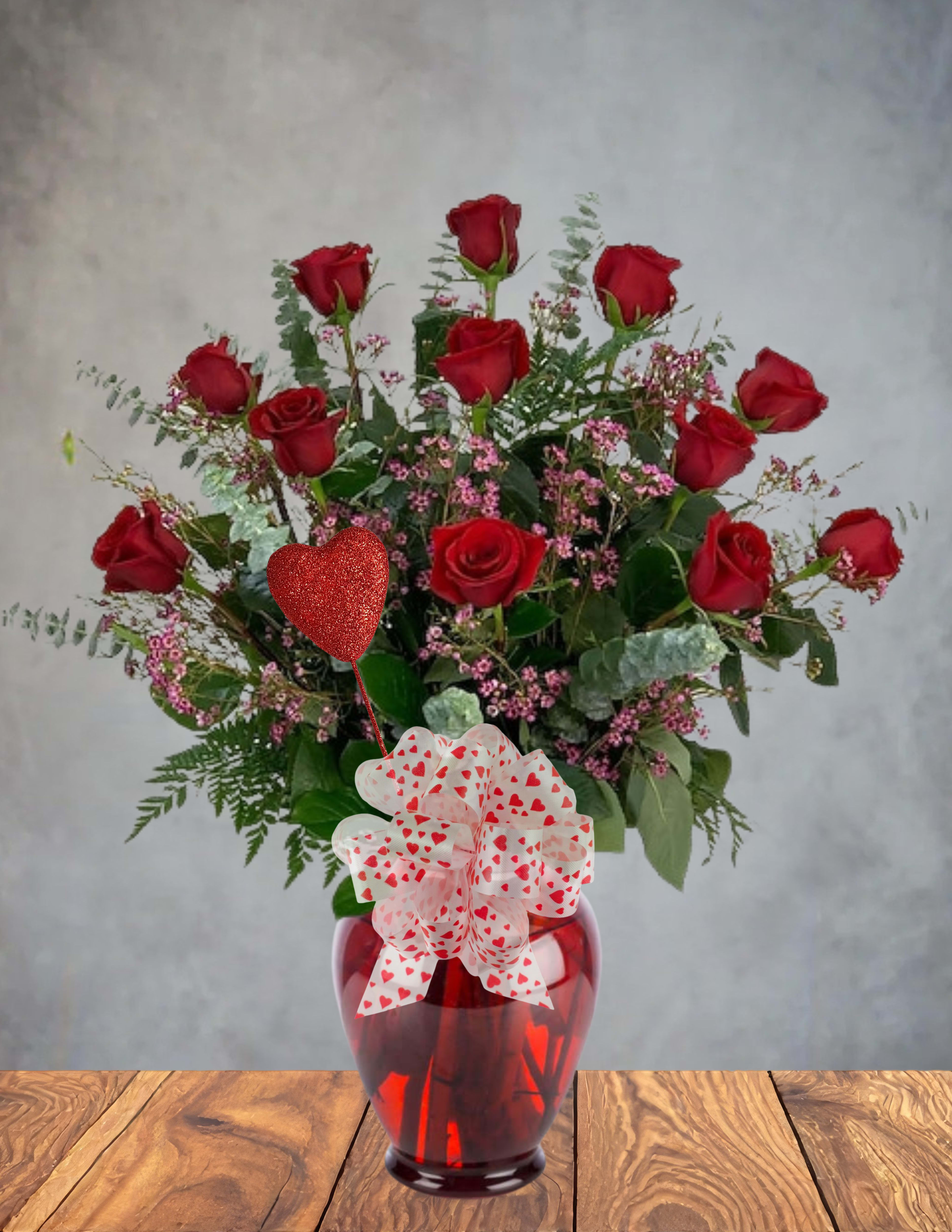 Red roses in a red glass vase with a heart-patterned bow and balloon