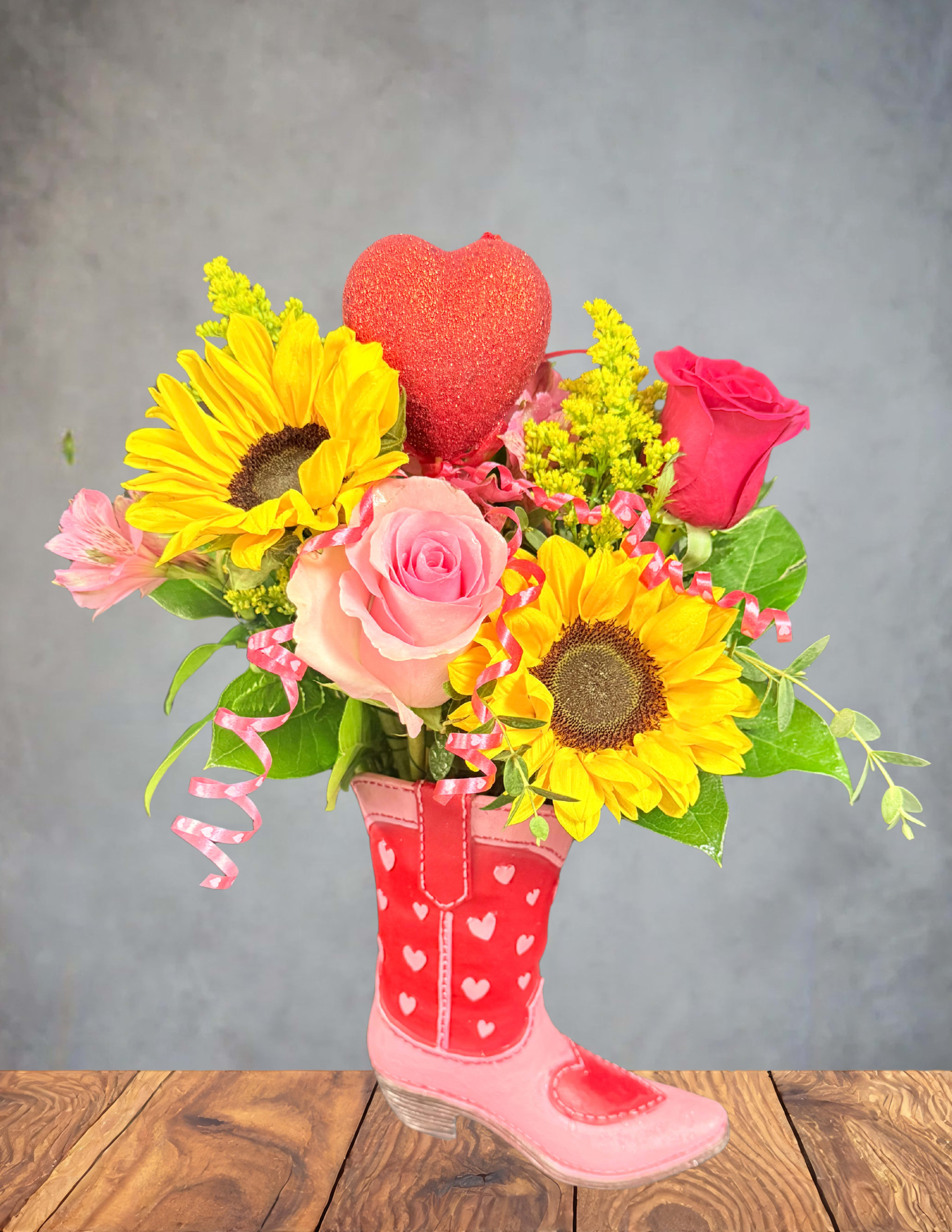 Bouquet of sunflowers and pink roses in a pink boot vase with a heart topper