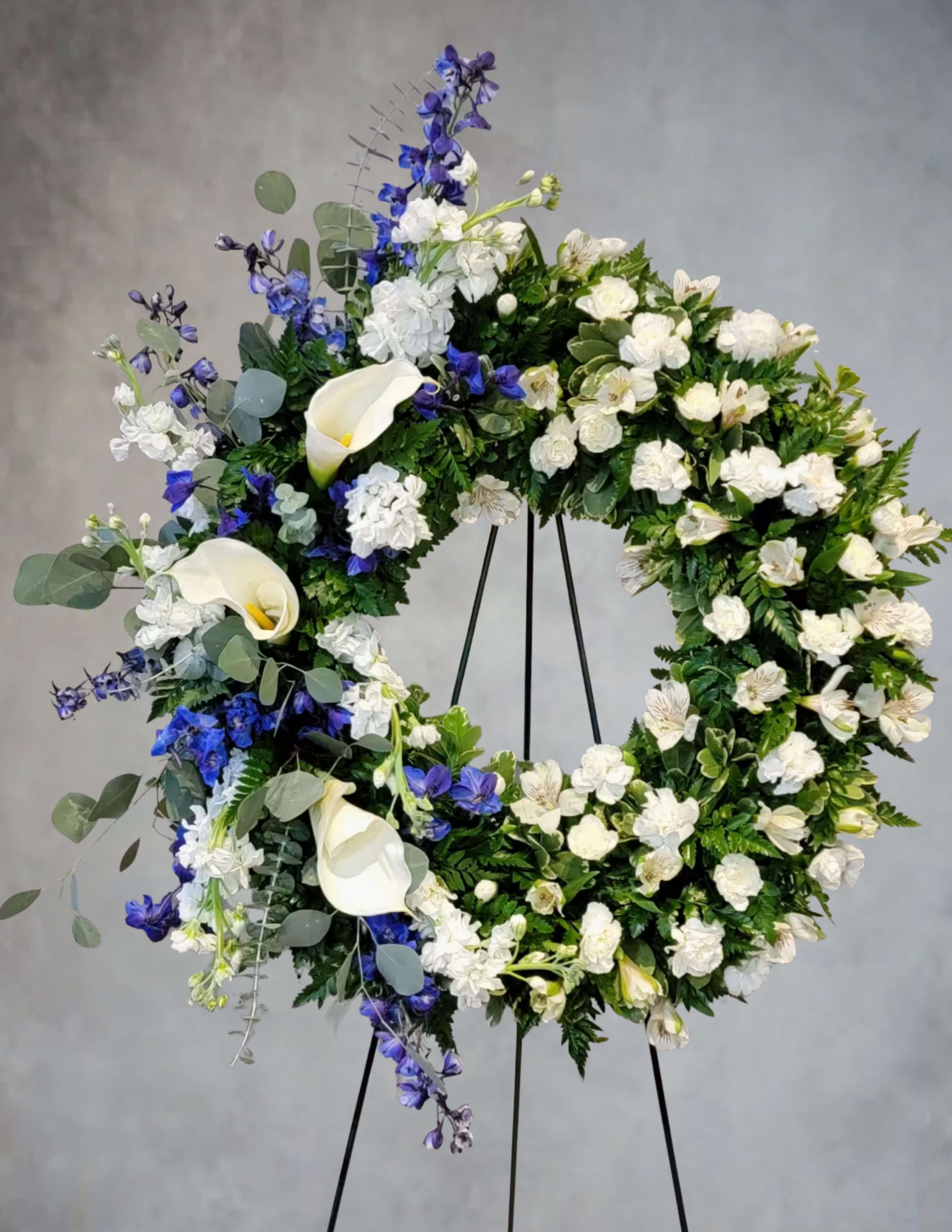 Large floral wreath with white calla lilies and blue flowers on a stand