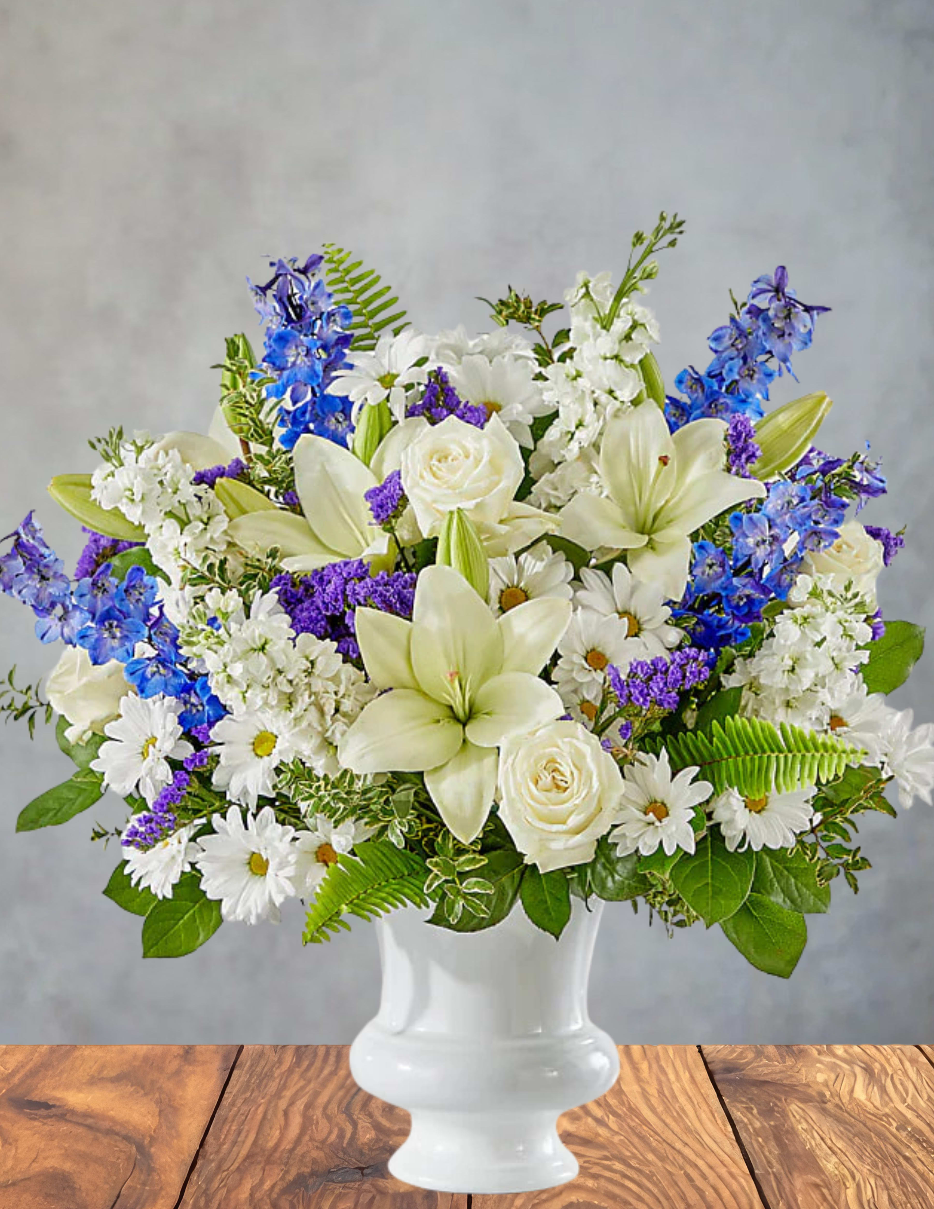 White lilies, roses, daisies, and blue flowers in a white vase