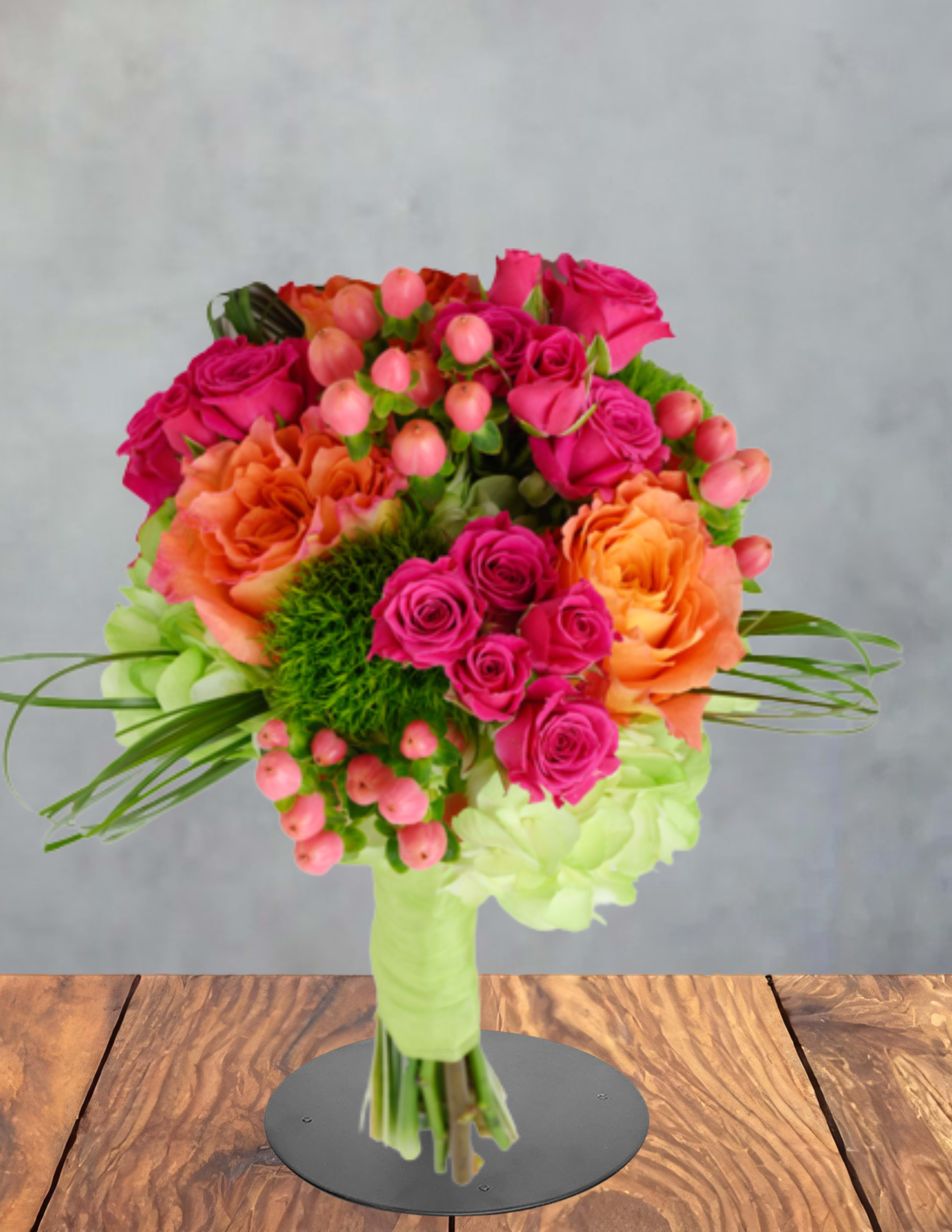 Orange and pink Prom Bouquet  - Vivid hot-pink and tangerine roses take center stage in this prom bouquet, creating a bold, celebratory look perfect for prom, anniversaries, or a joyful birthday surprise. The bright contrast of pink and orange immediately reads as festive and youthful, so the person you're thinking of will feel noticed and radiant the moment they see it.  A compact, rounded hand-tied arrangement features saturated hot-pink and orange roses nestled over a pale green hydrangea base, accented with clusters of small pink berry-like blooms and touches of white and green foliage. The stems are finished with a light green wrap and tied with ribbon for a polished presentation that's easy to carry and wear.  Ideal for young recipients or anyone who loves color-forward bouquets, this arrangement works beautifully as a prom corsage alternative, congratulations gift, or romantic surprise that says "celebrate today." Care is simple: keep stems trimmed and fresh water supplied if placed in a vase after the event, and order in time to ensure peak blooms for the occasion.