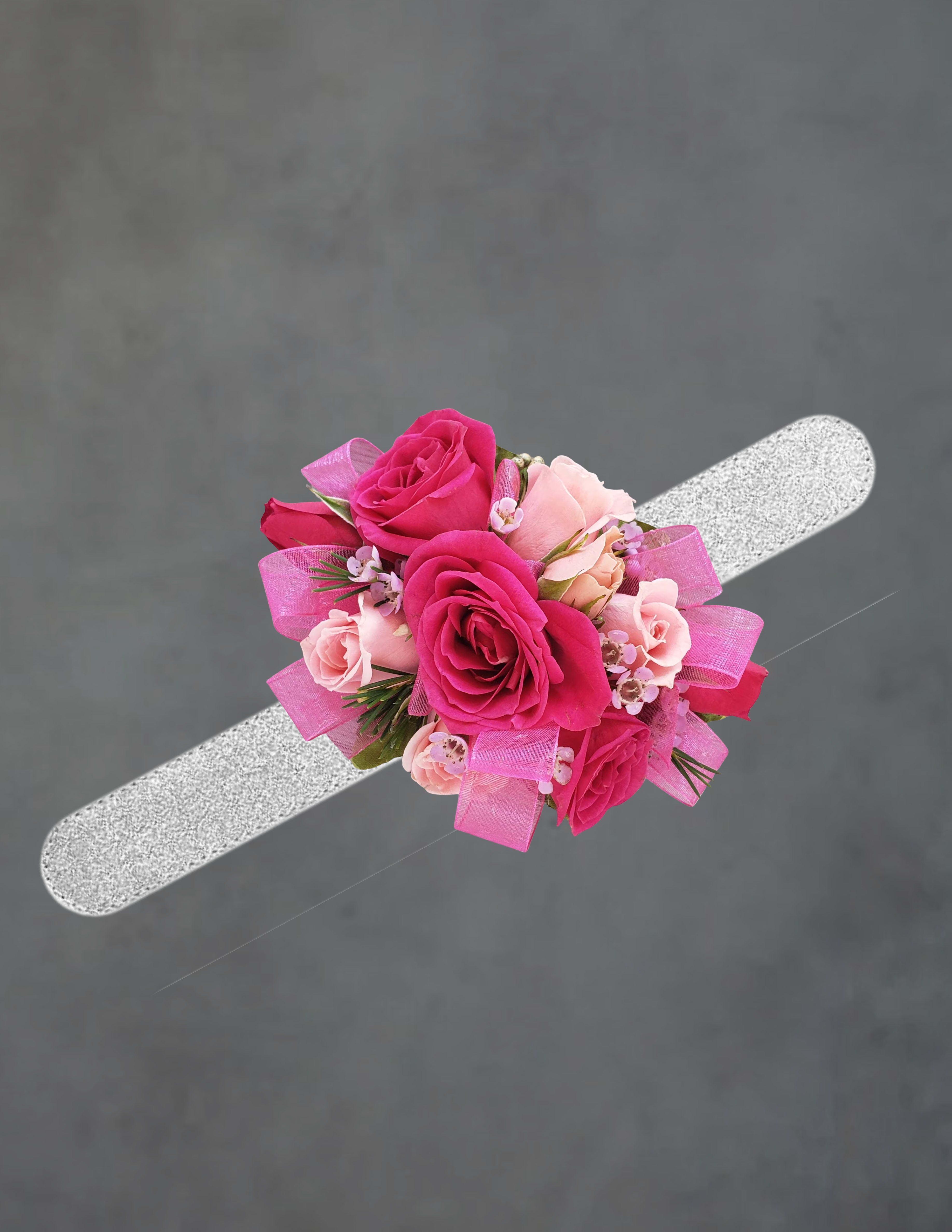pink corsage - Clustered pink roses-from hot pink to soft blush-sit snugly on a silver wristband to create a romantic pink corsage perfect for prom or a wedding. The compact, wearable arrangement reads as feminine and cheerful, the bright pink ribbon adding a polished, festive finishing touch that makes the person you're gifting feel celebrated and camera-ready.  Small accent blooms and narrow greenery weave around the roses to add texture and movement while keeping the silhouette tidy and comfortable for the wrist. The corsage pairs roses with complementary small florals in white and pink tones, secured to a durable silver wristband that's easy to wear and adjust. Its petite scale keeps it elegant on a bride, bridesmaid, or a prom-goer who wants a classic, pretty accessory.  Made to be noticed without overwhelming the outfit, this corsage is ideal for formal events where the recipient should feel special and seen. To keep it fresh, store in a cool place and mist lightly before wearing; order in advance to match party colors and ensure ribbon placement.
