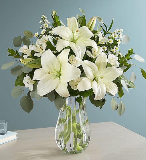 White lilies and small white daisies in a clear glass vase