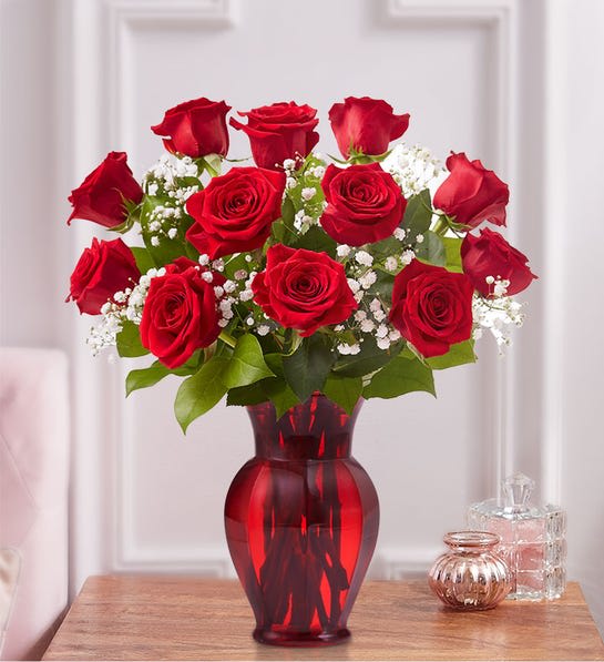 Red roses arranged in a red glass vase with white filler flowers