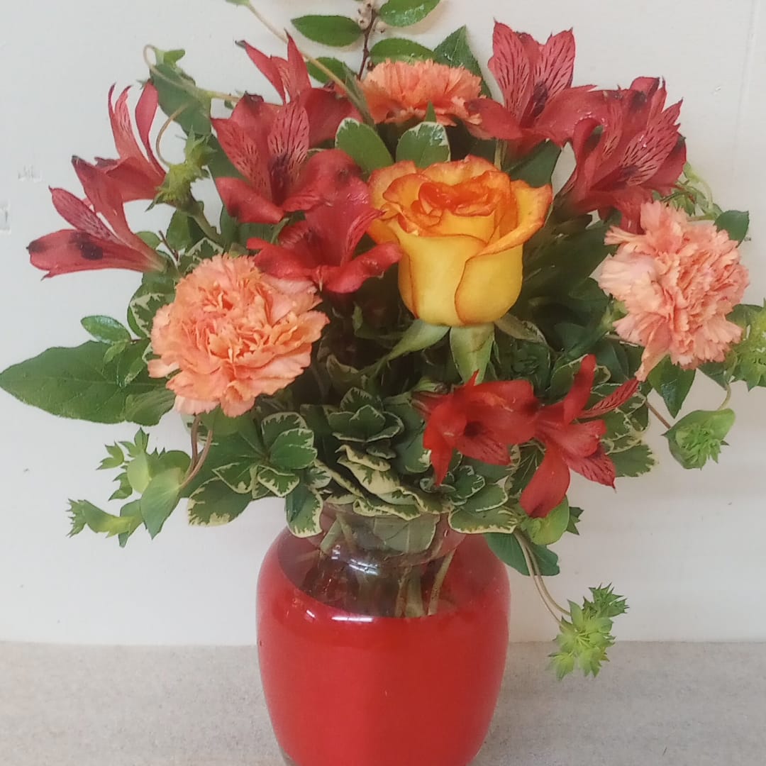 Mixed bouquet of red and peach flowers in a red glass vase