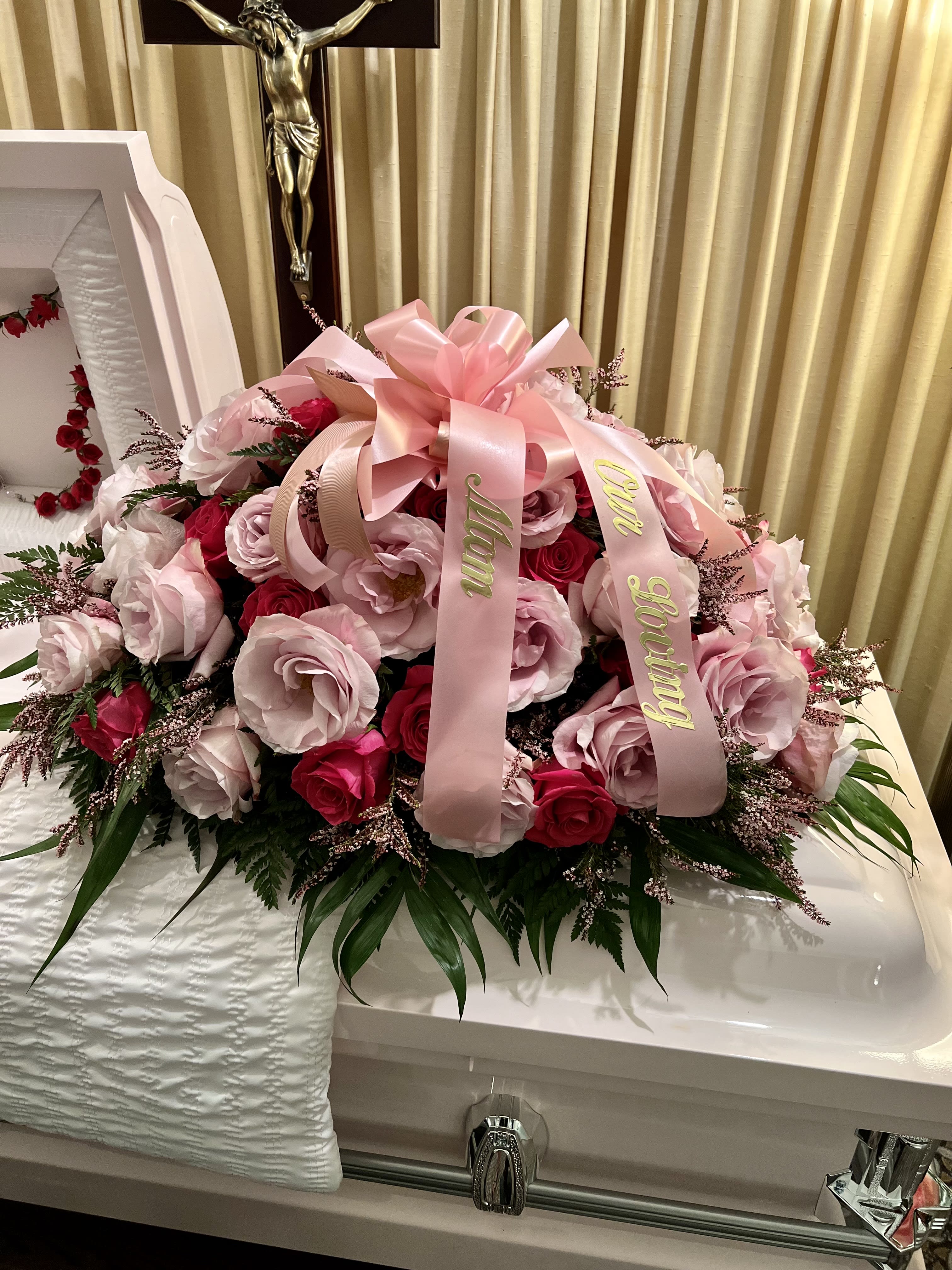 Pink and red rose arrangement on a white casket with a pink ribbon.