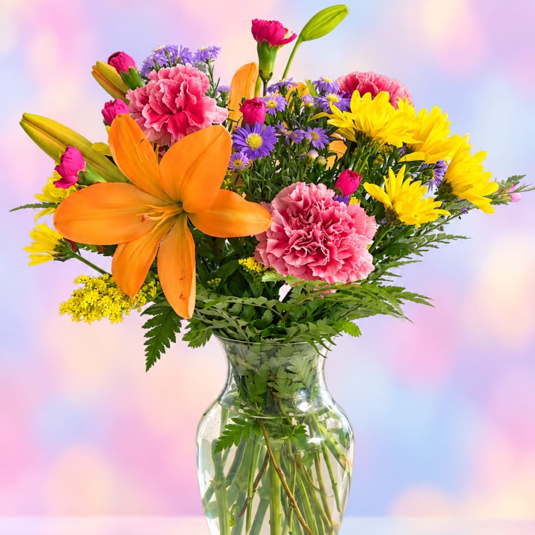 Mixed bouquet of orange lilies, pink carnations, and yellow daisies in a glass vase