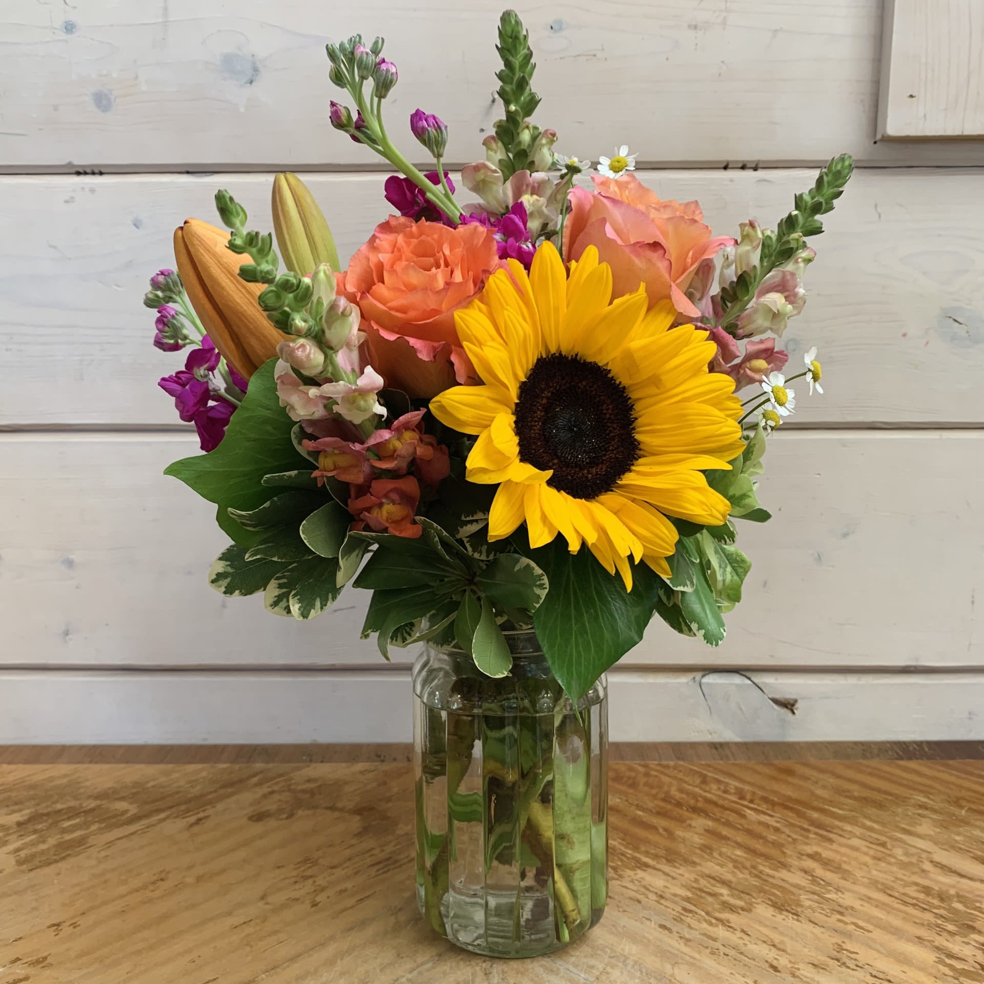 Bouquet of sunflowers, orange roses, and purple blooms in a glass vase