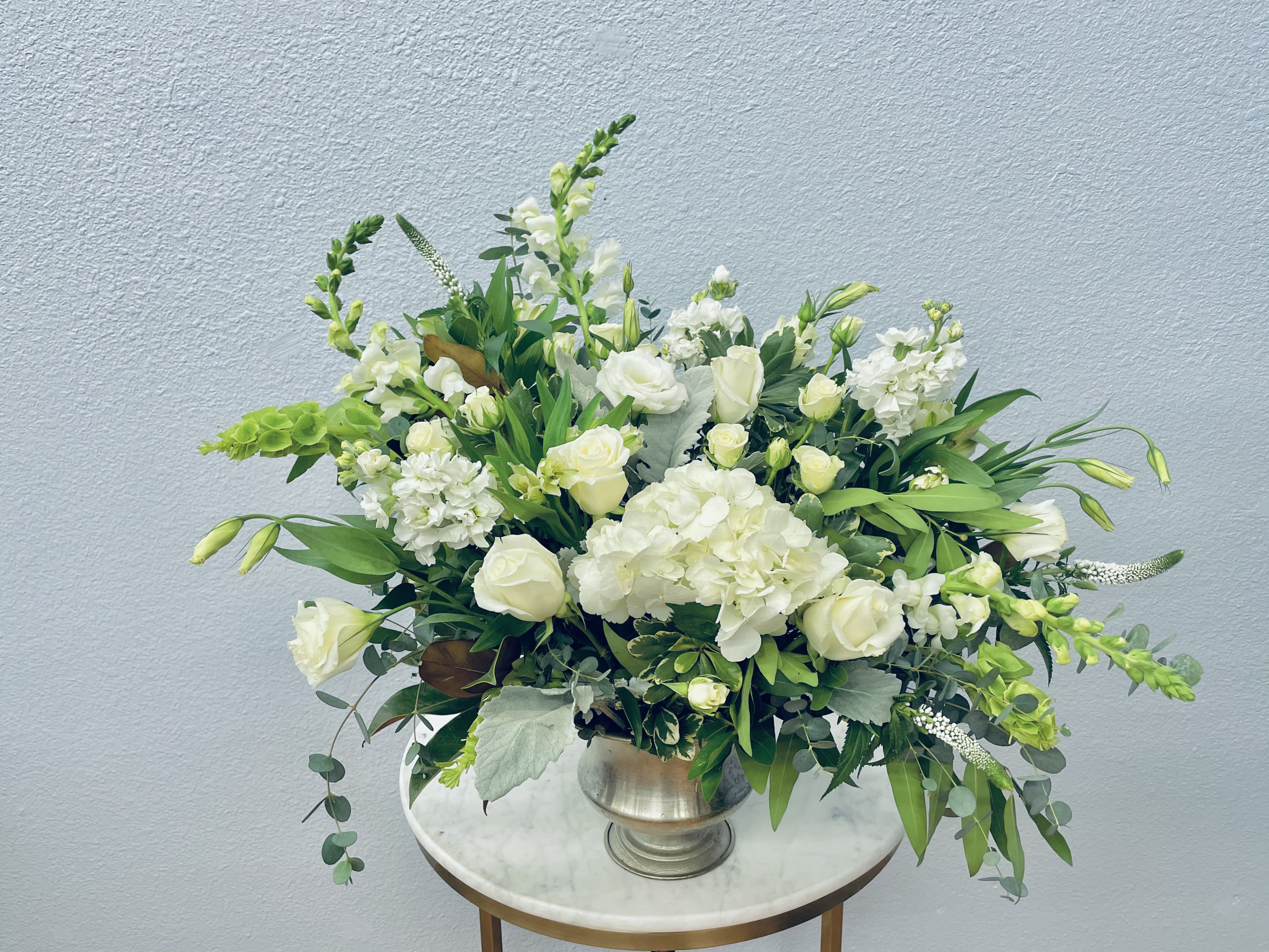 White floral arrangement in a silver vase with green accents