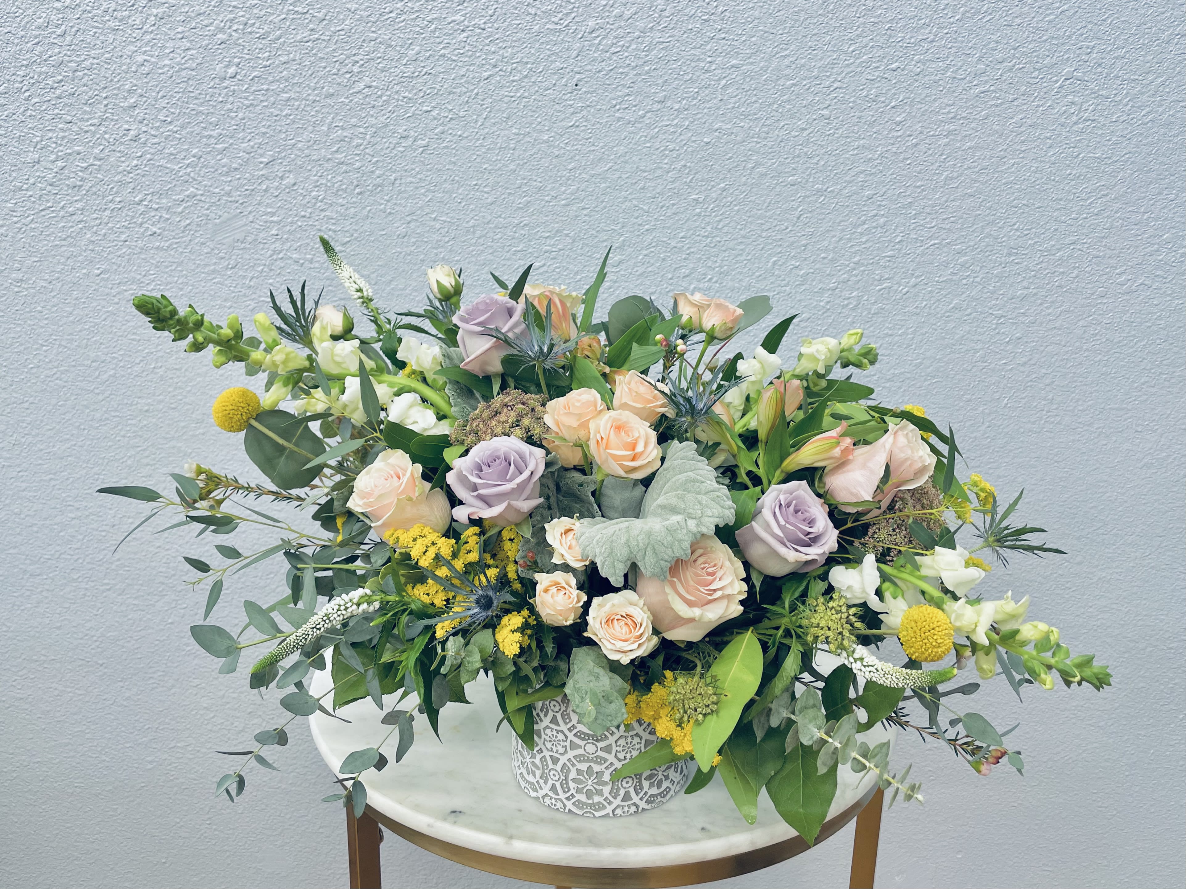 Mixed bouquet of pastel roses and yellow blooms in a decorative white vase