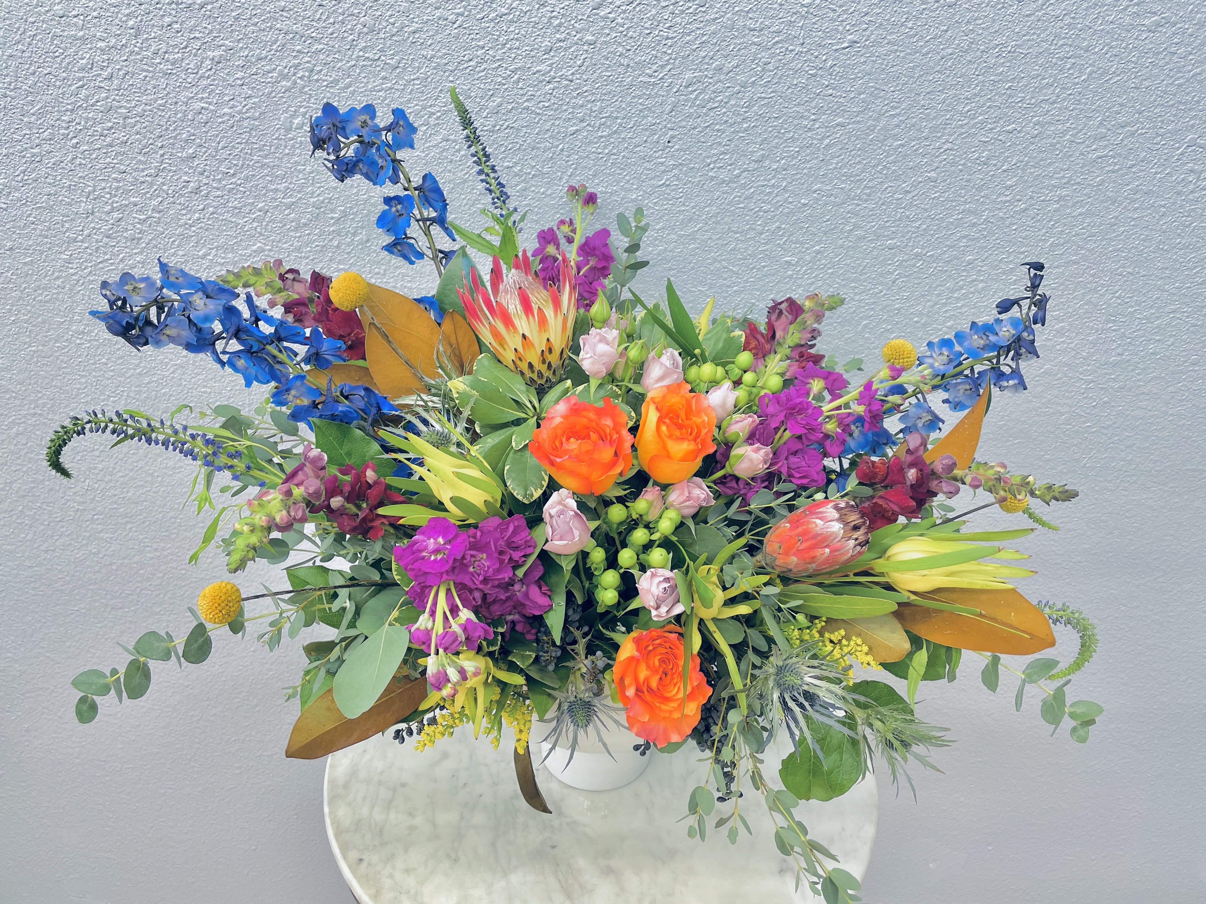 Bright mixed bouquet with orange roses, blue flowers, and pink blooms in a white vase