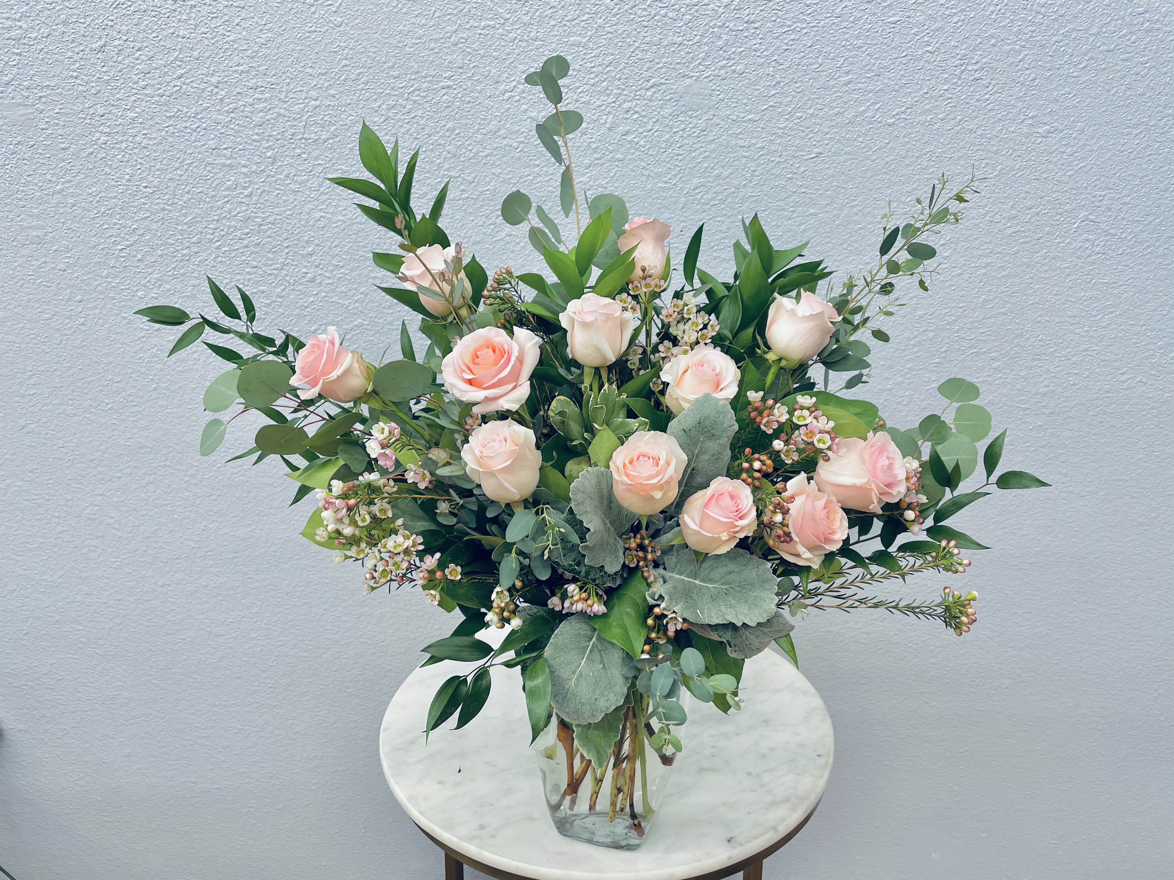 Soraya - Color Palette: pastel roses One dozen premium roses tucked into botanical eucalyptus and seasonal greens in a graceful glass vase.