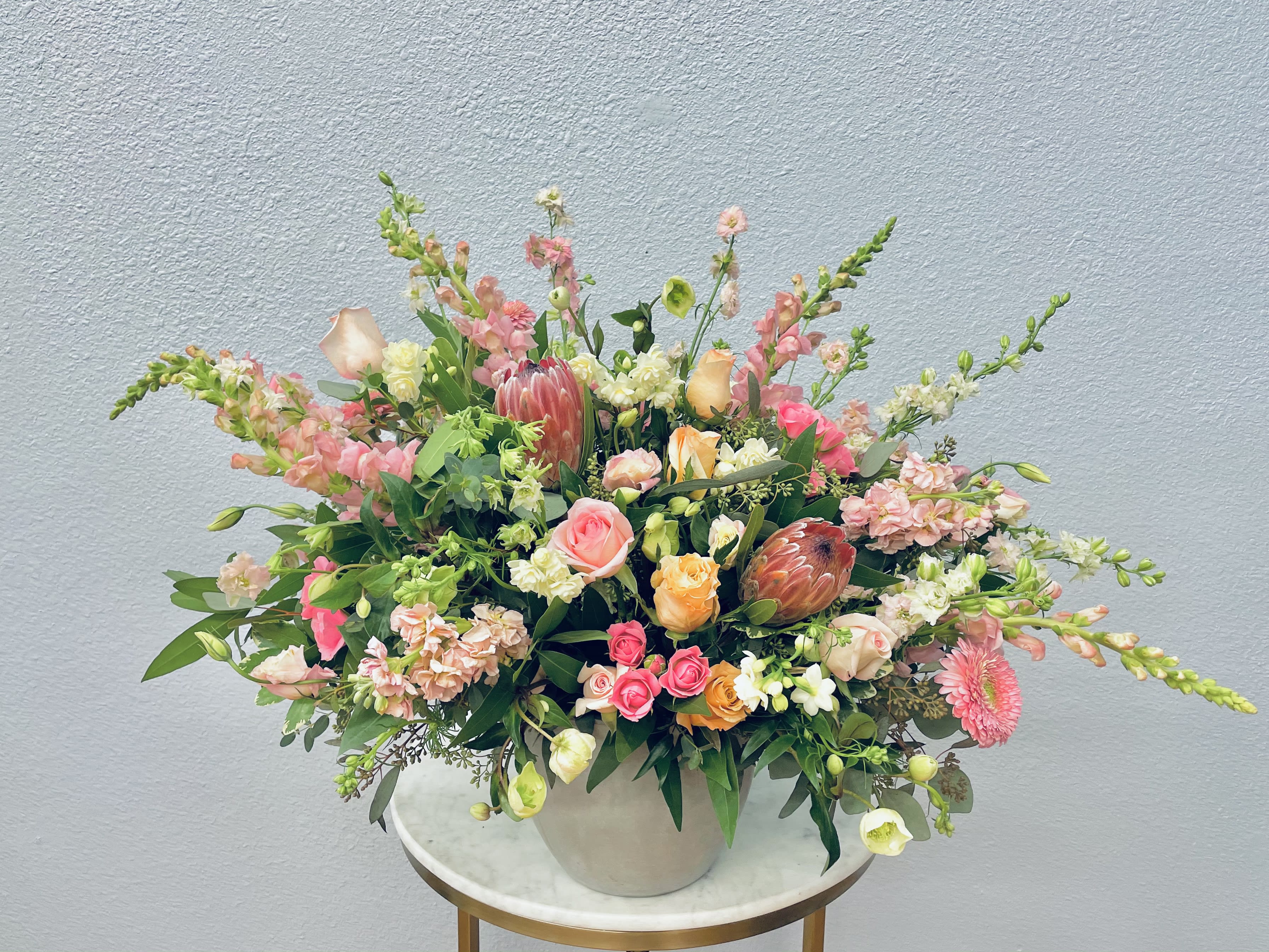 Large mixed floral arrangement in a white vase with pink, peach, and white blooms