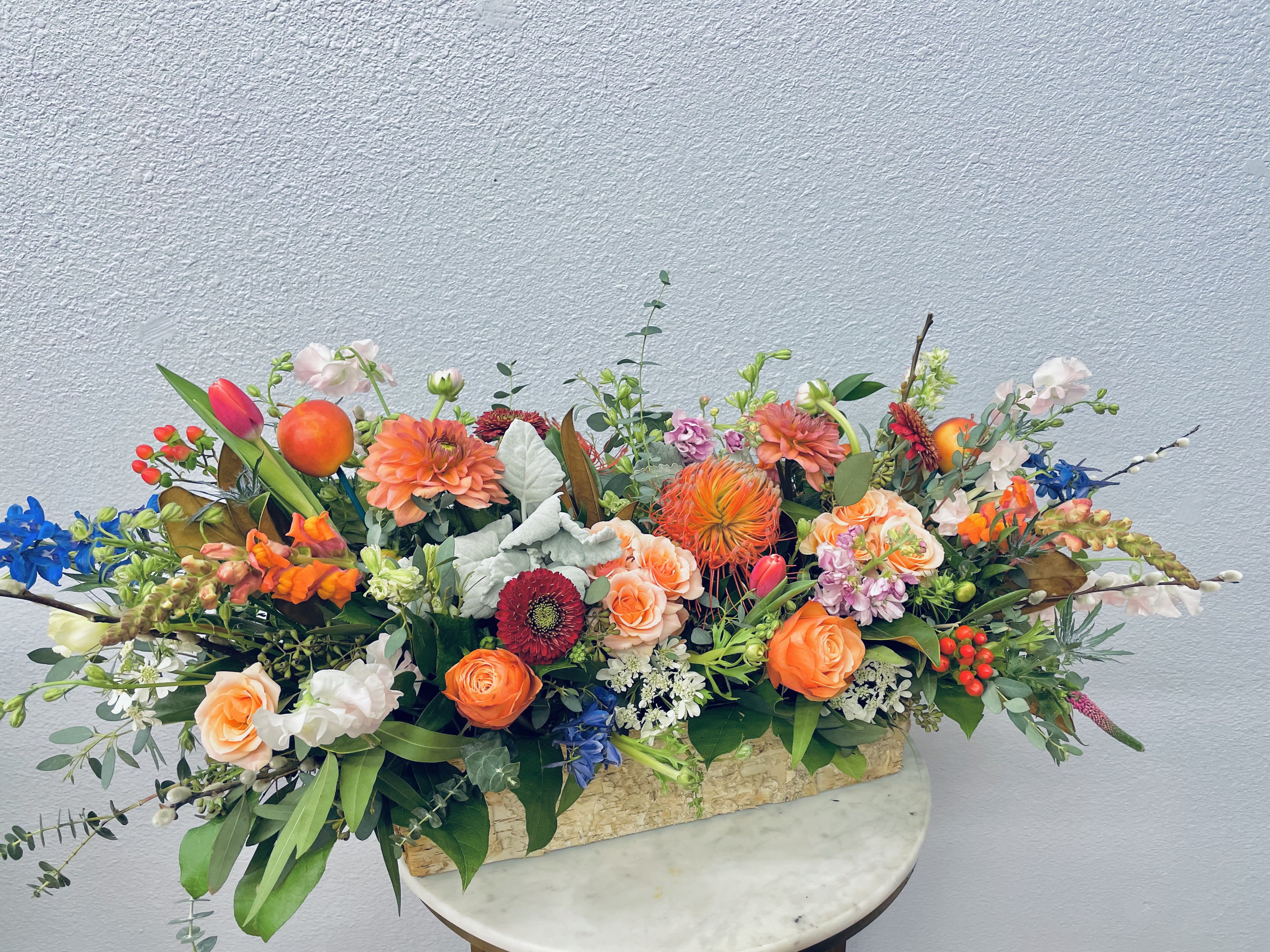 Low floral centerpiece with orange, pink, blue, and white blooms in a rectangular container