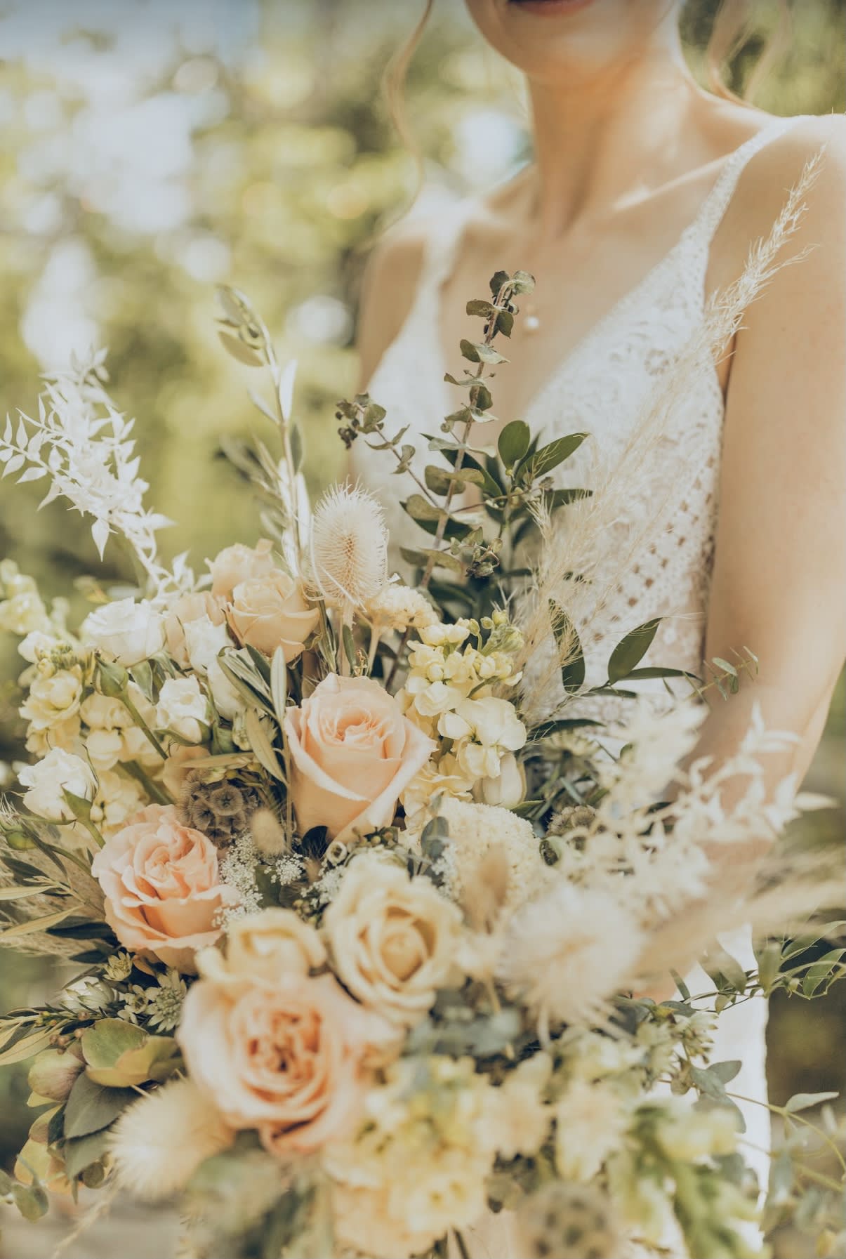 Bride holding a bouquet of peach and cream roses with airy dried accents