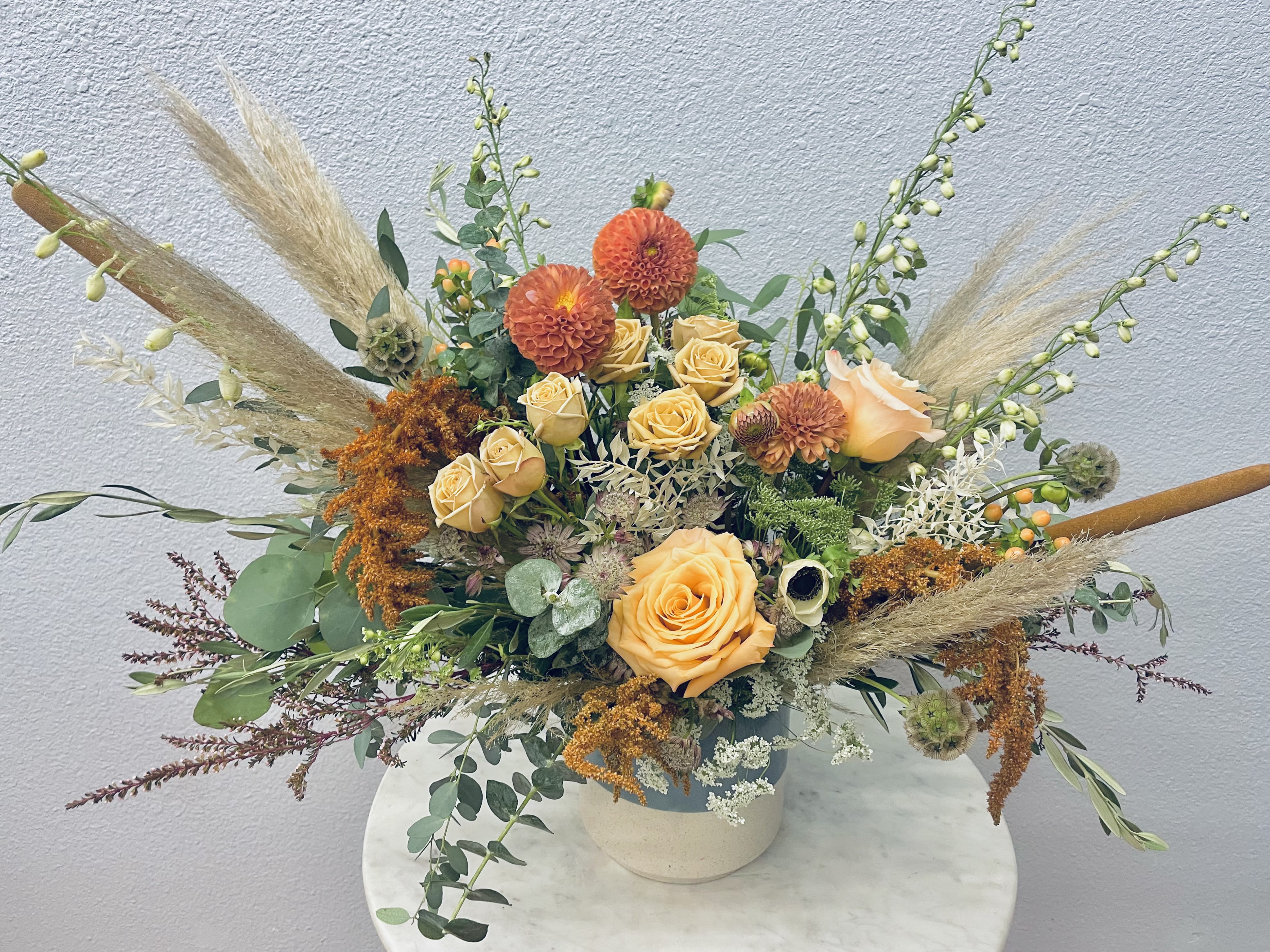 Orange roses and dahlias in a low vase with airy dried grasses