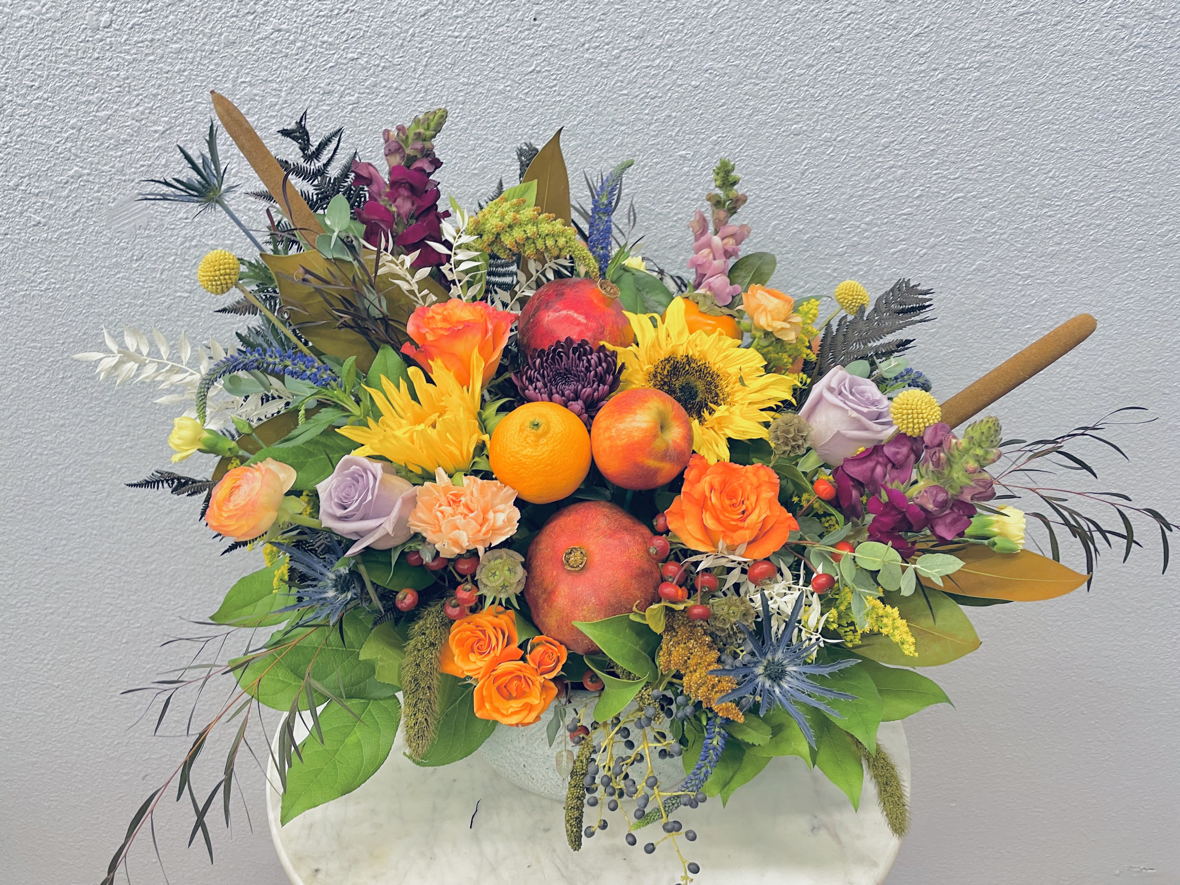 Colorful fruit and flower arrangement in a white vase