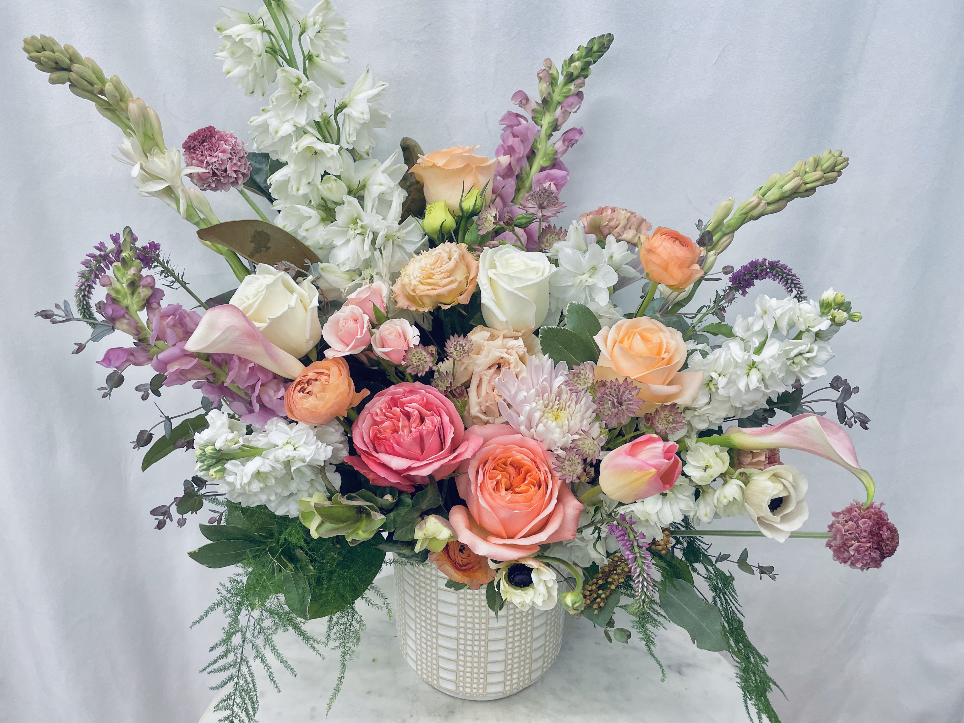 Mixed bouquet of roses, calla lilies, and snapdragons in a white vase