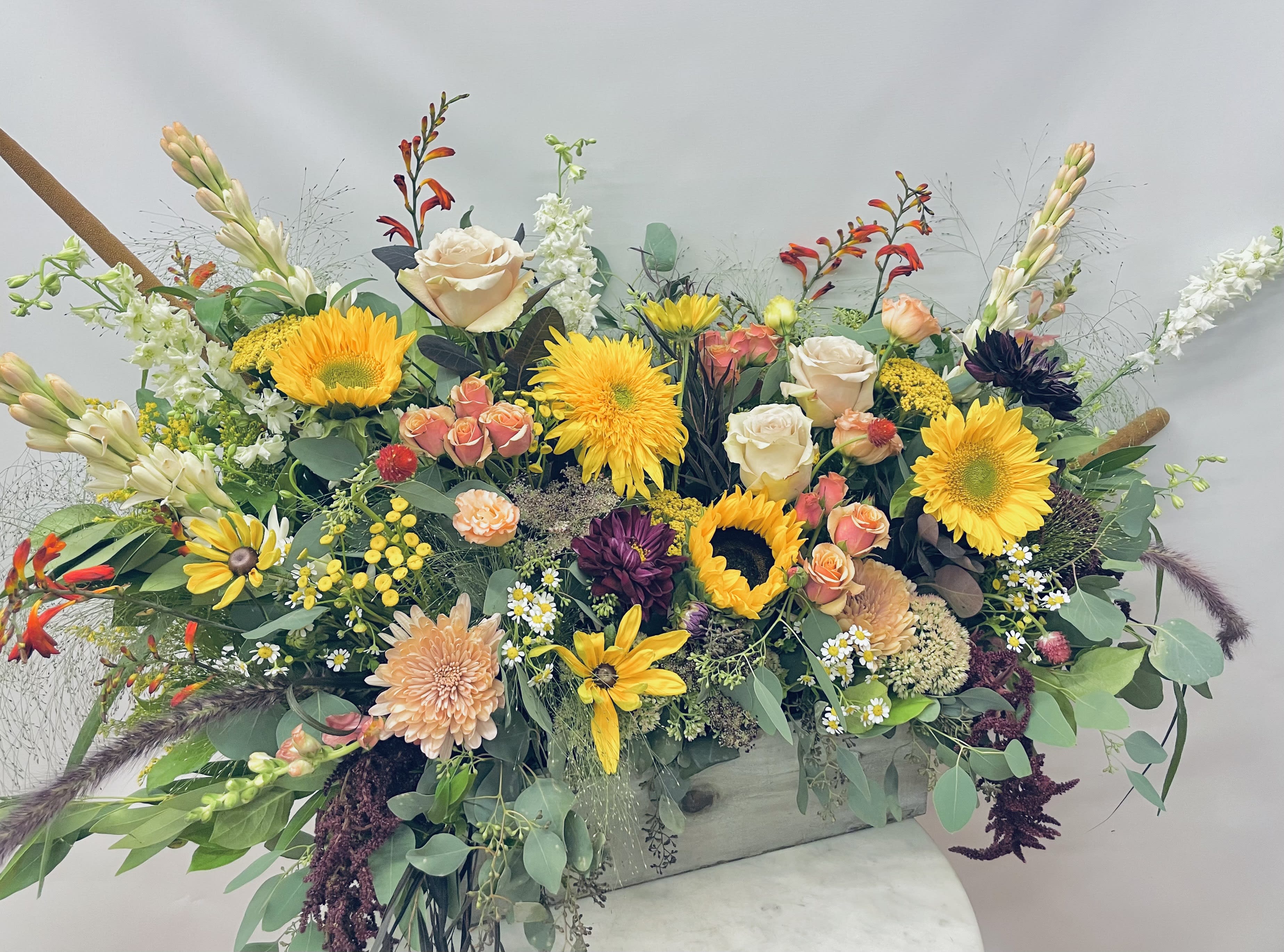 Large mixed flower arrangement with sunflowers, roses, and daisies in a rectangular container
