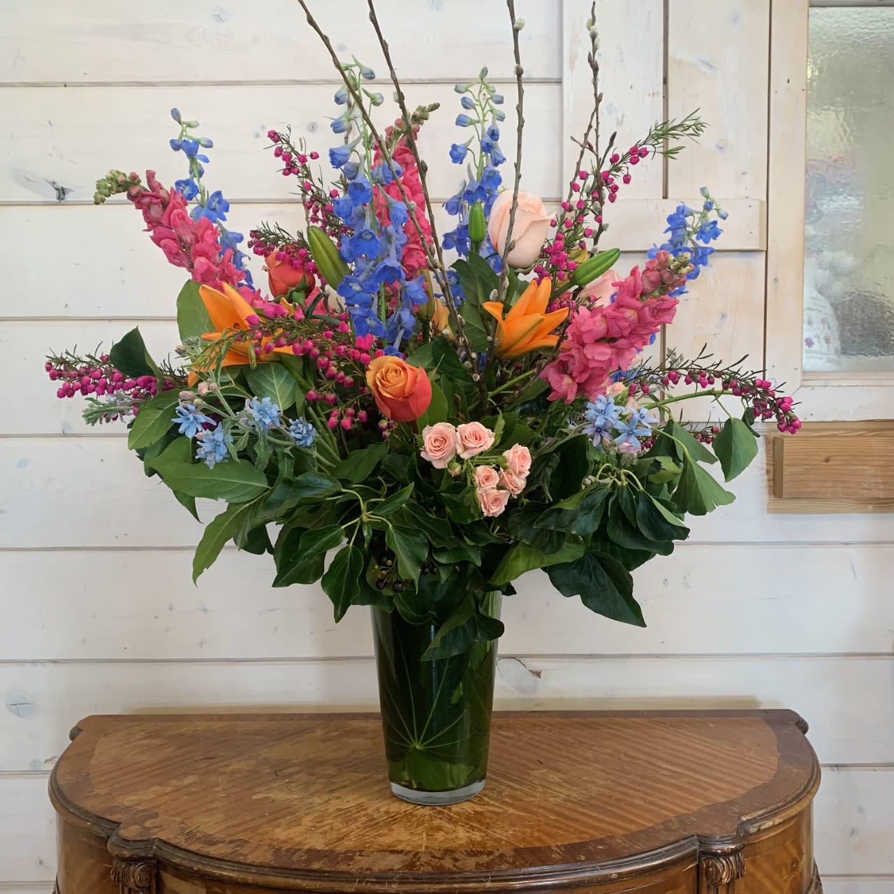 Tall mixed bouquet in a glass vase with blue, pink, orange, and peach flowers