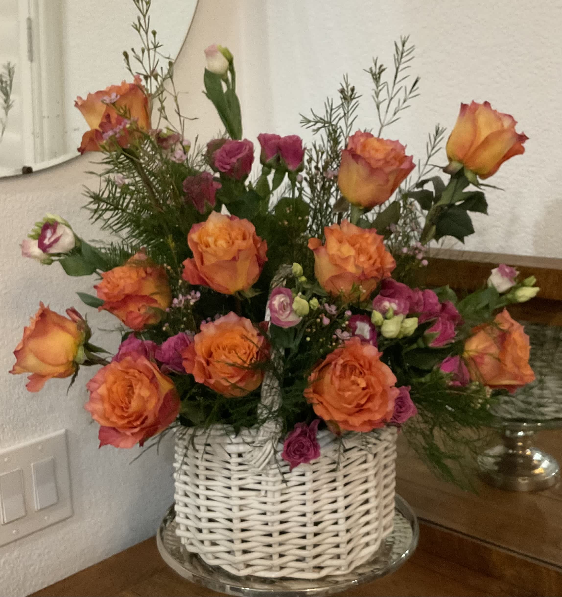 Orange and pink roses arranged in a white wicker basket