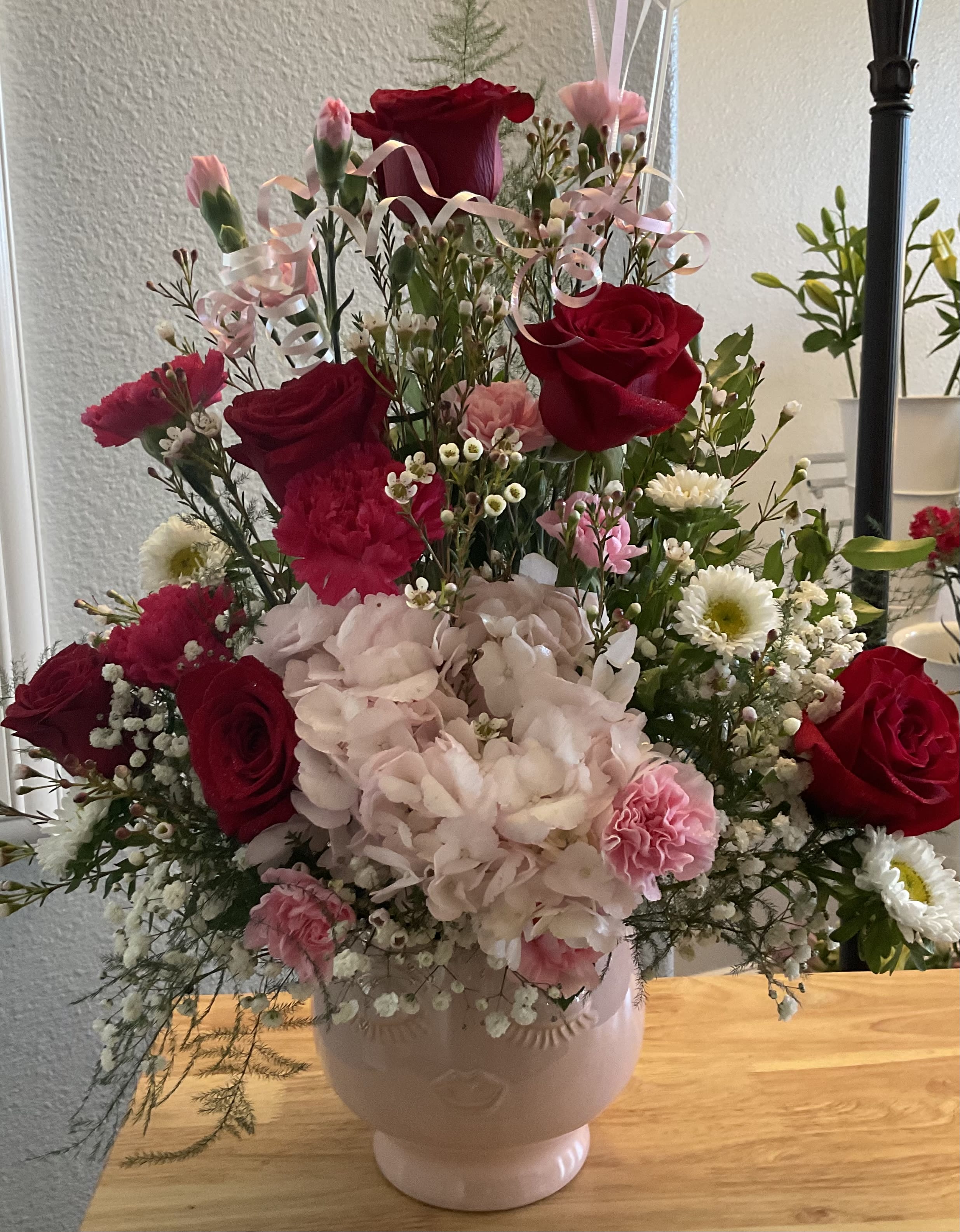 Pink and red floral arrangement in a pale vase with ribbon accents