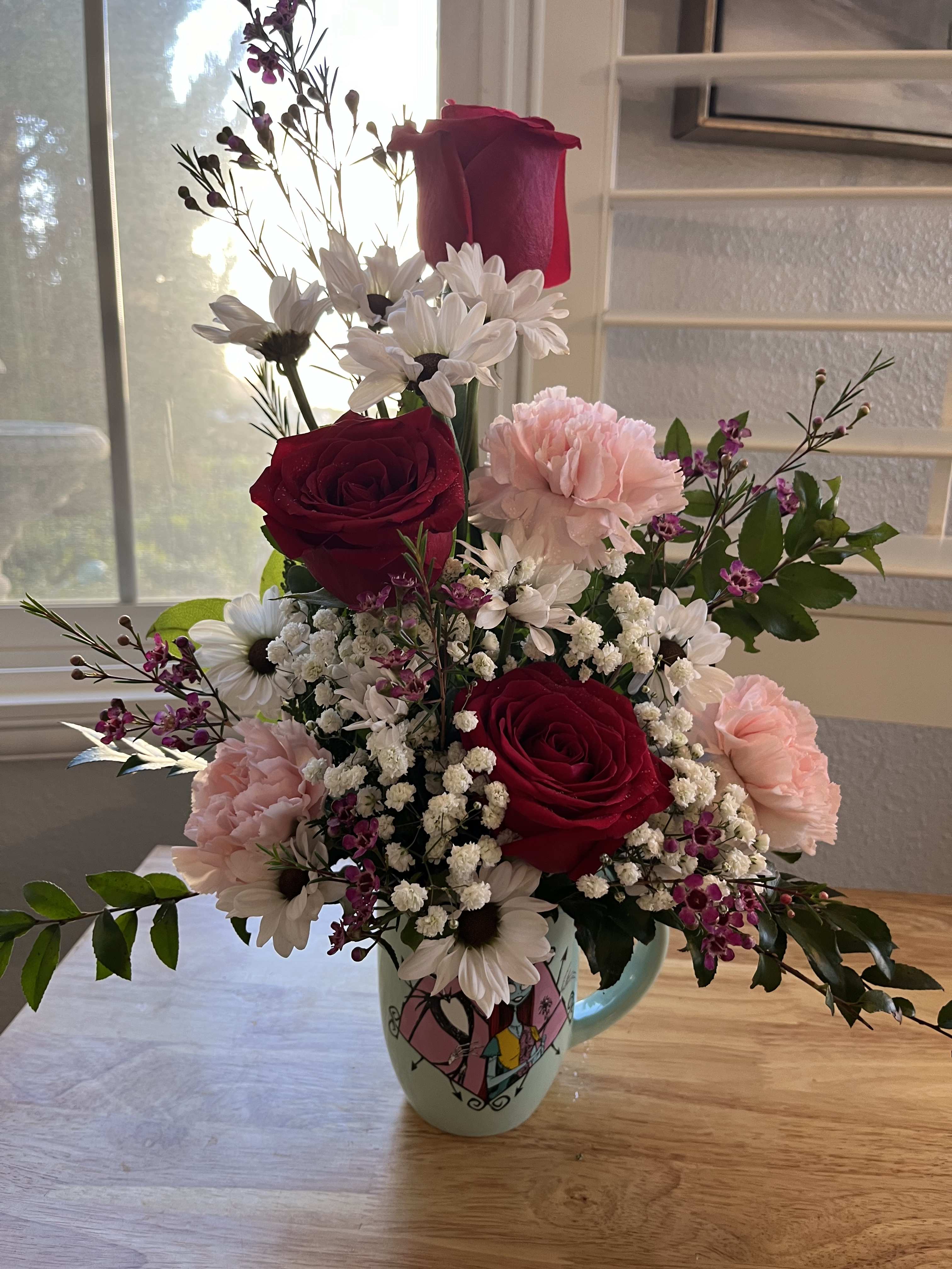 Mixed bouquet of red roses, pink carnations, and white daisies in a mug