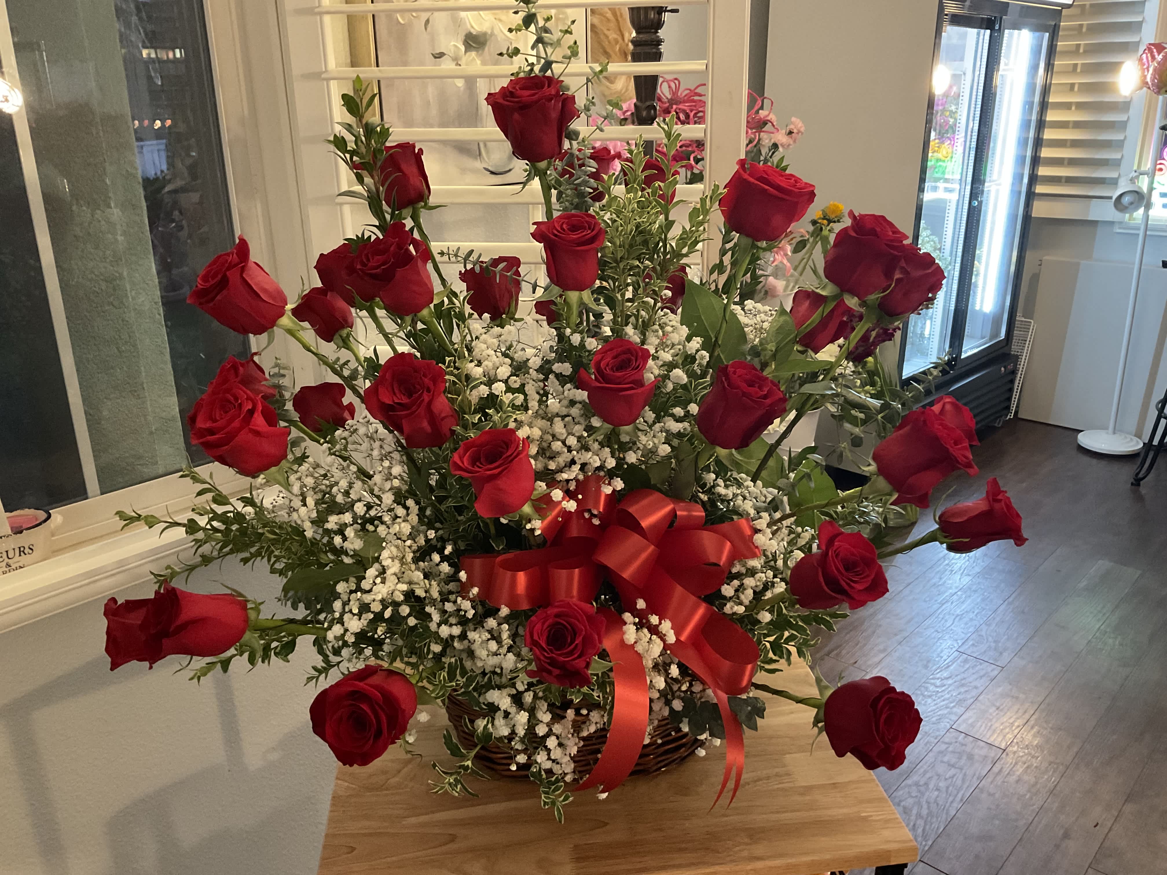 Basket arrangement of red roses with baby's breath and a red ribbon