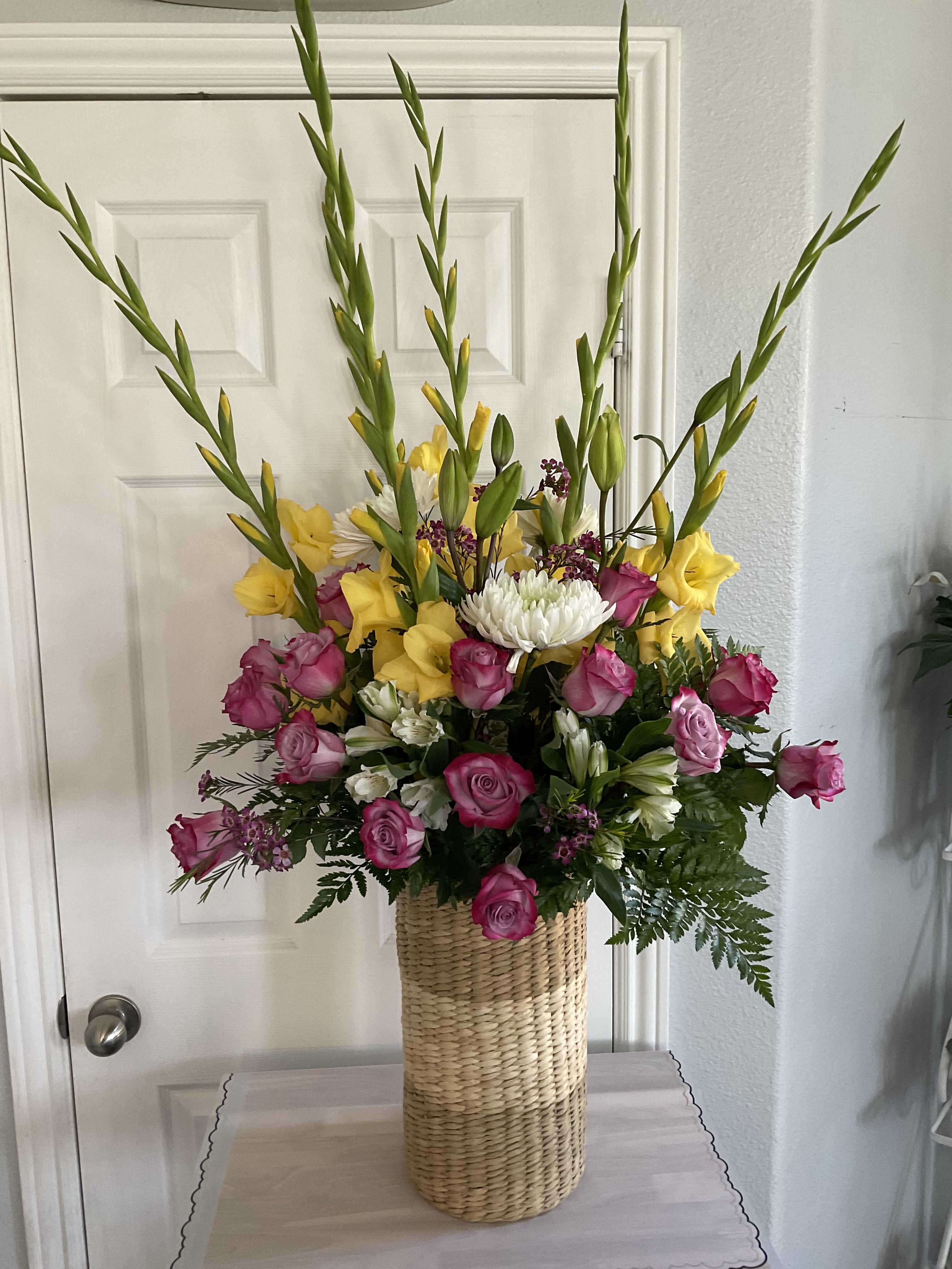 Tall mixed bouquet of pink and yellow flowers in a woven basket vase