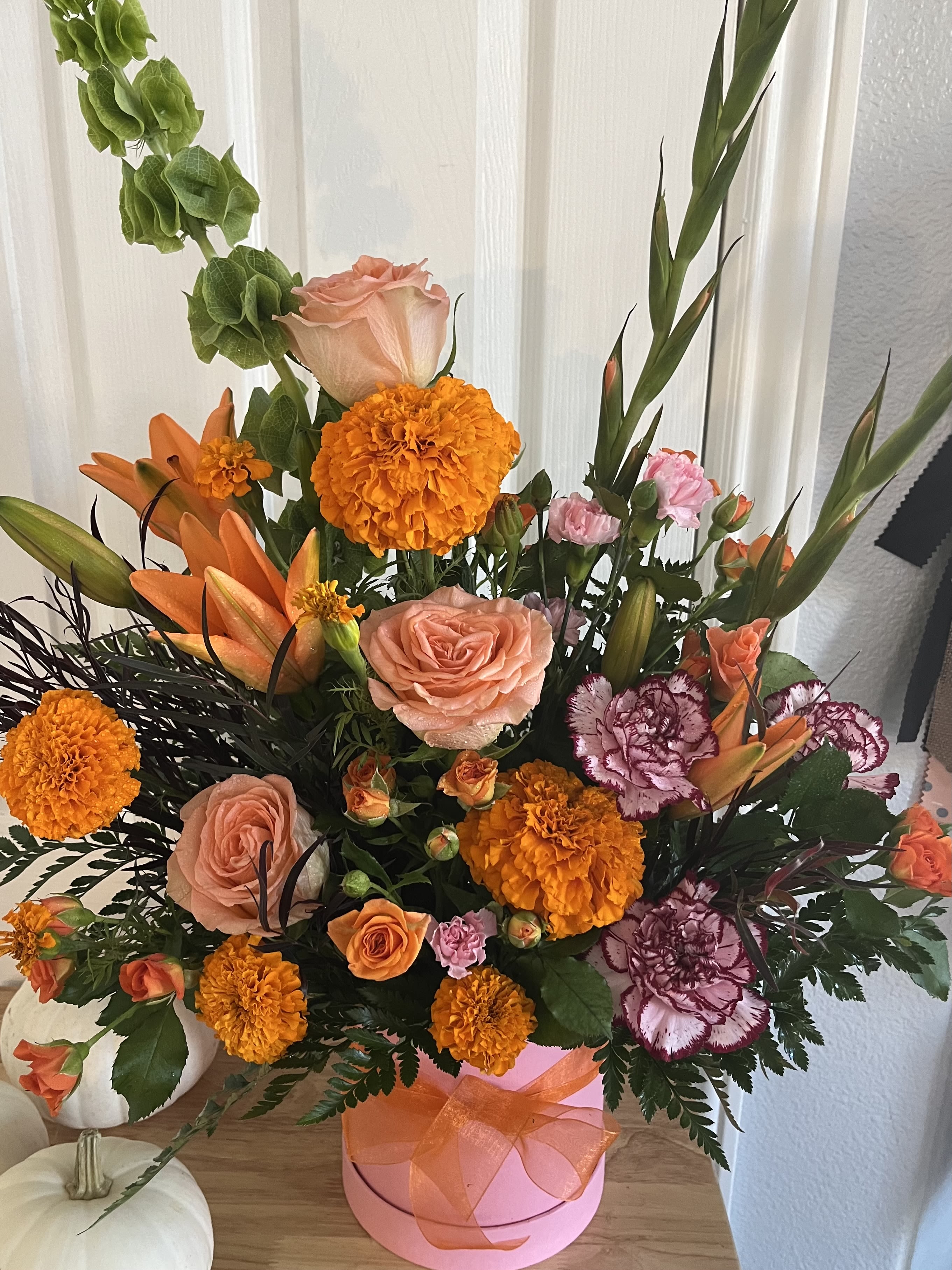 Orange and peach floral arrangement in a pink hatbox with ribbon