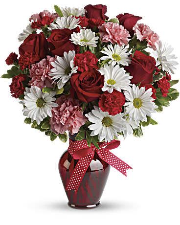 Red roses, white daisies, and pink carnations in a red vase with a ribbon