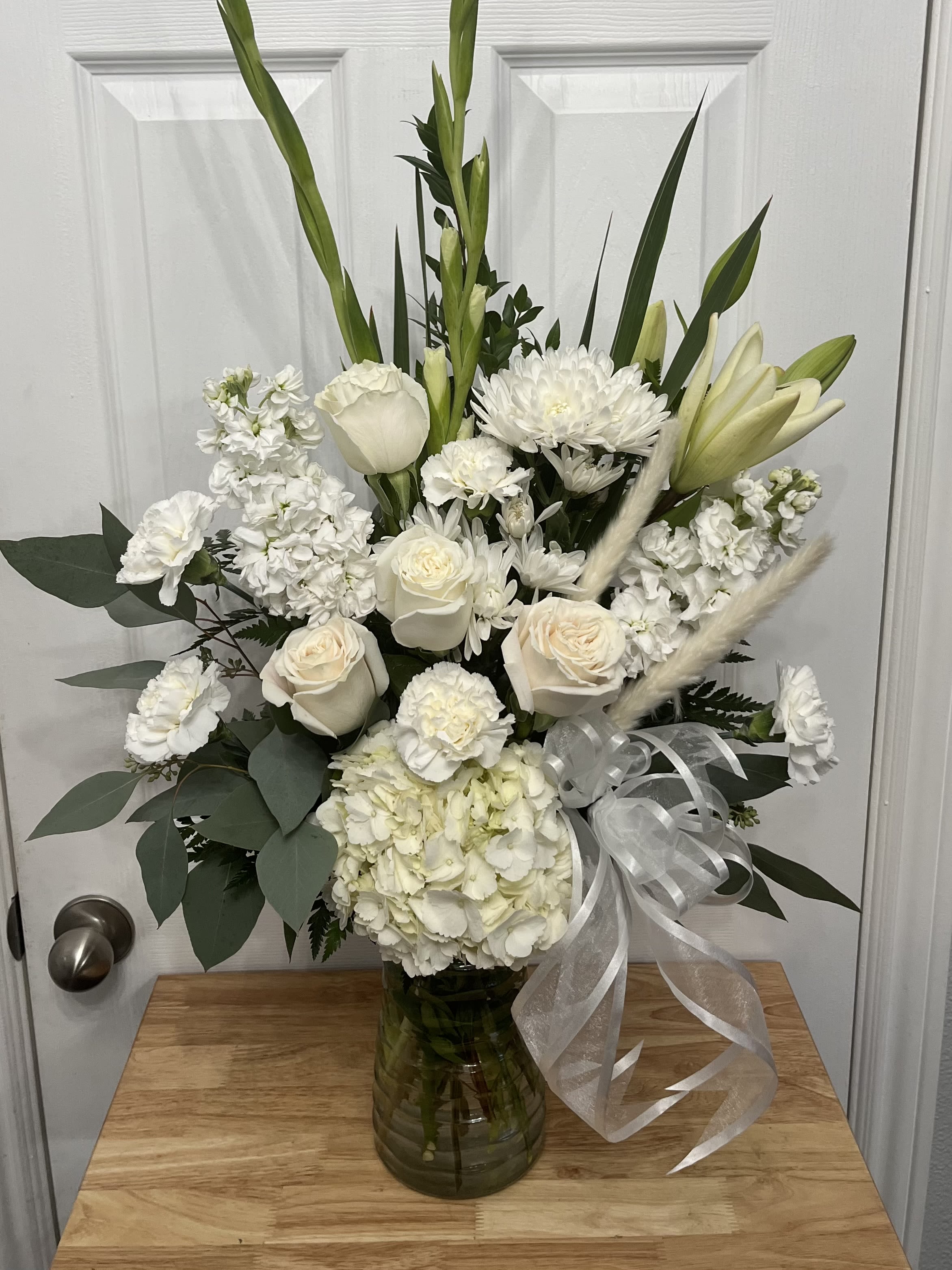 White floral arrangement in a glass vase with ribbon